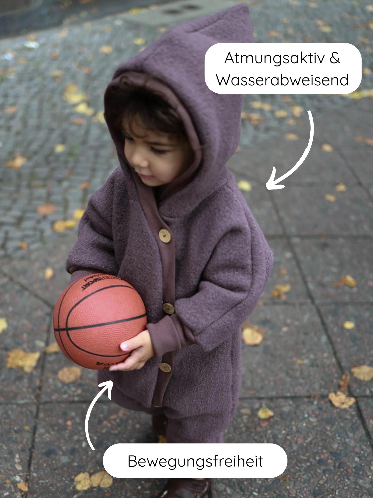 Kleinkind in Kuschelanzug Wollwalk - Malve, steht auf nassem Gehweg, hält Basketball. Atmungsaktiv, wasserabweisend, mit Bewegungsfreiheit, ideal für Kita und Spaziergänge. Handgefertigt in Berlin.