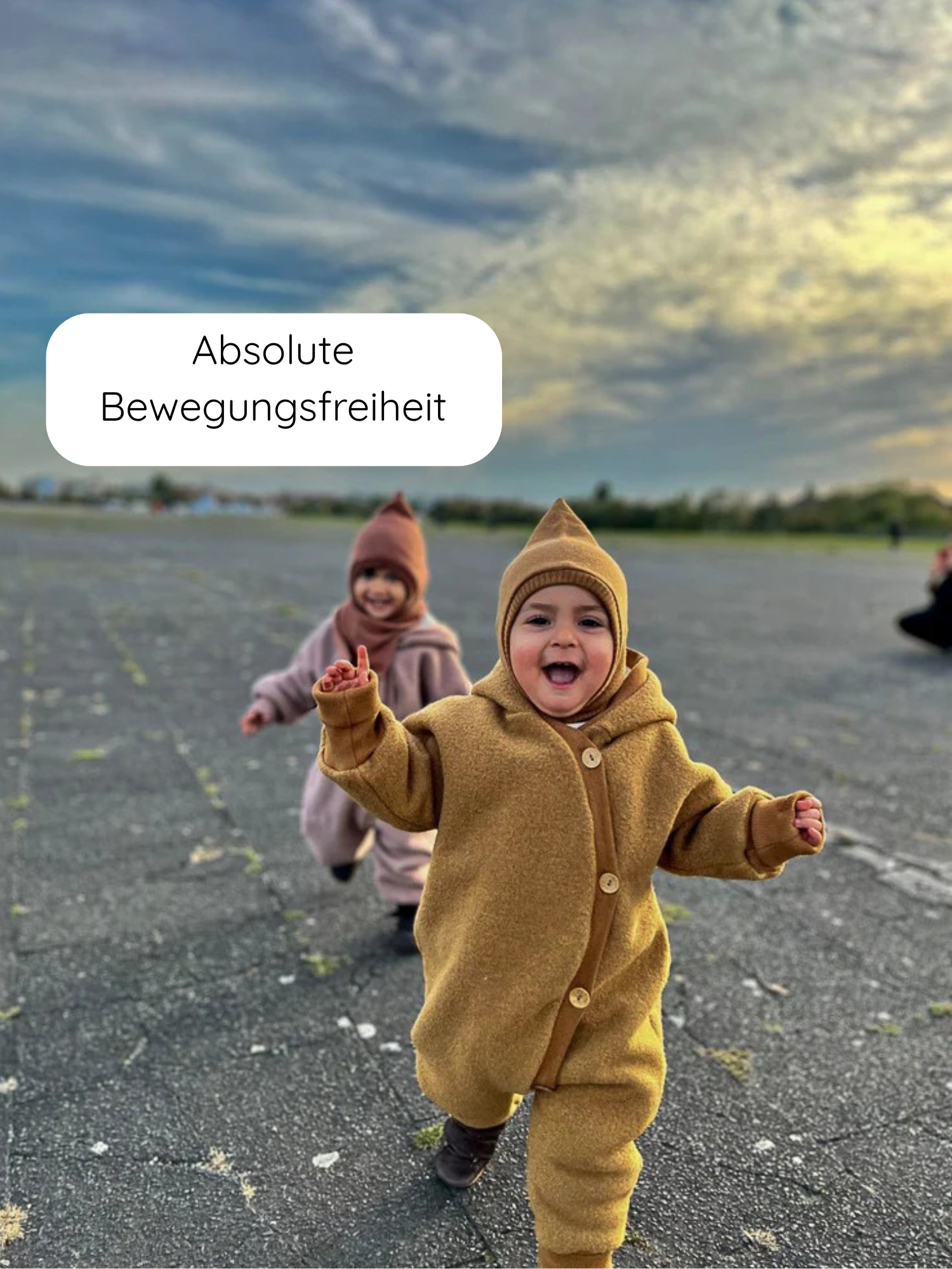 Zwei Kleinkinder rennen in Wollwalk Overalls mit Teddyfutter. Der Overall in Honigfarbe bietet Bewegungsfreiheit und Schutz. Perfekt für kalte Tage, handgefertigt in Berlin aus Bio-Materialien.