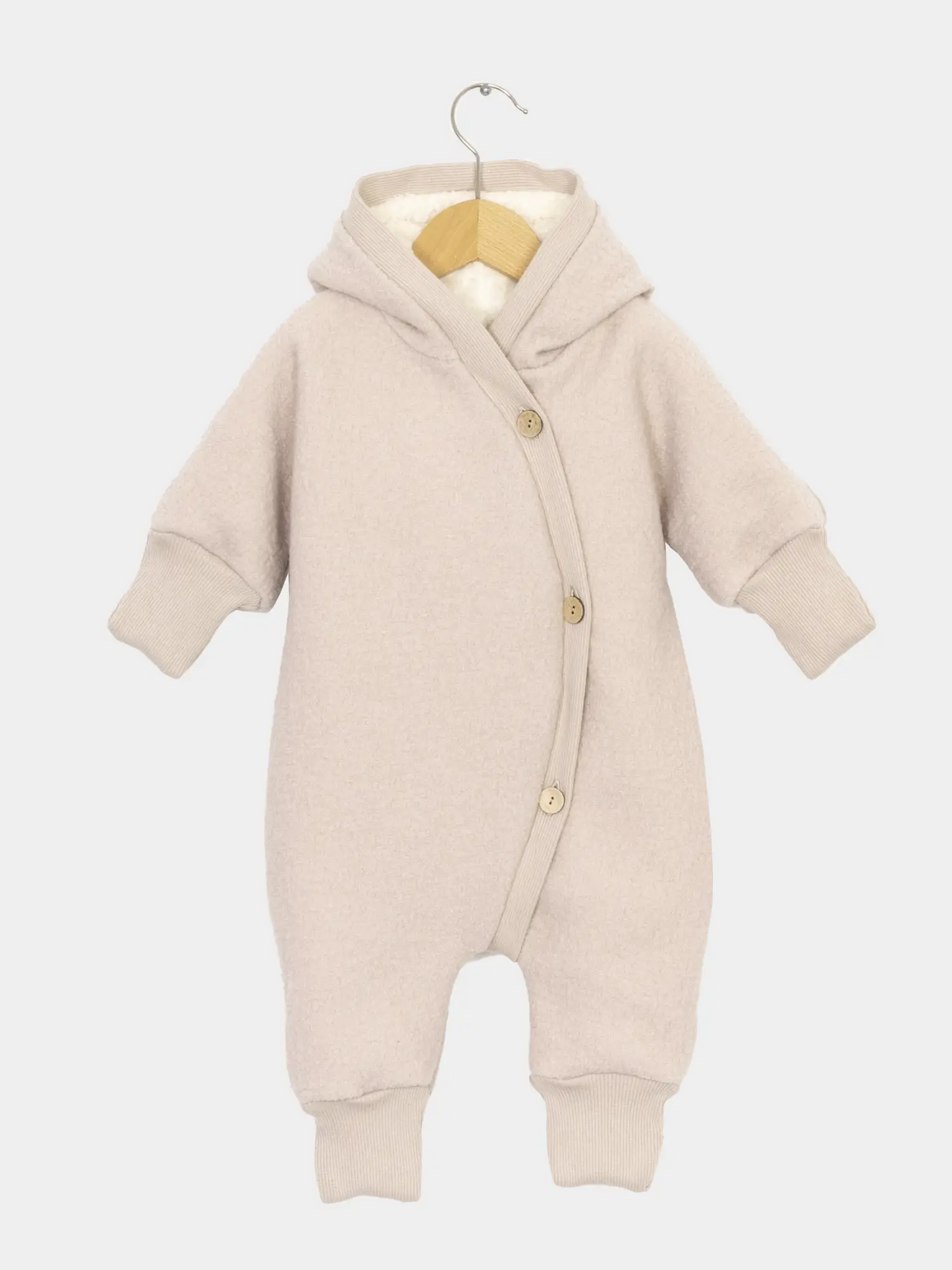 Teddy-Kuschelanzug Wollwalk - Sand: Schneeanzug für Kinder und Babys mit Kapuze, langen Ärmeln und Knopfleiste, aus weichem Wollwalk und Teddyfutter, auf einem kleinen Holzkleiderbügel präsentiert. Ideal für kalte Tage.
