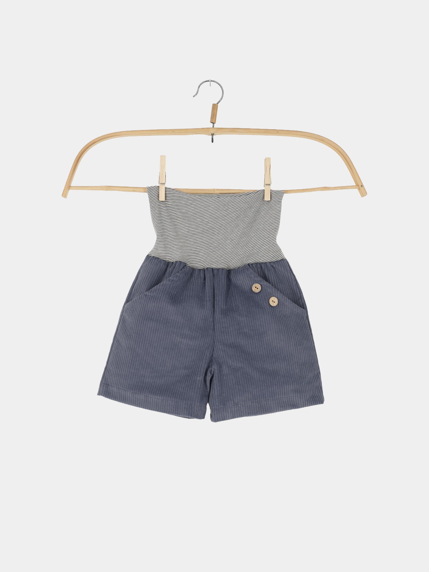 Kurze Buxe Breitcord - Jeansblau: Kinder-Einteiler mit blauen Cordshorts und zwei Holzköpfen, dazu grauweiß gestreiftes Tube-Oberteil, hängend an einem Holzkleiderbügel, perfekt für Abenteuer.
