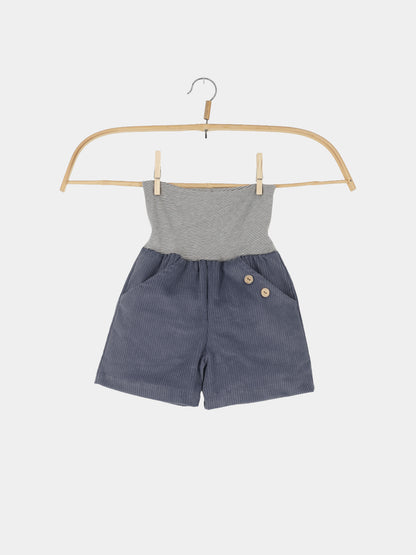 Kurze Buxe Breitcord - Jeansblau: Kinder-Einteiler mit blauen Cordshorts und zwei Holzköpfen, dazu grauweiß gestreiftes Tube-Oberteil, hängend an einem Holzkleiderbügel, perfekt für Abenteuer.