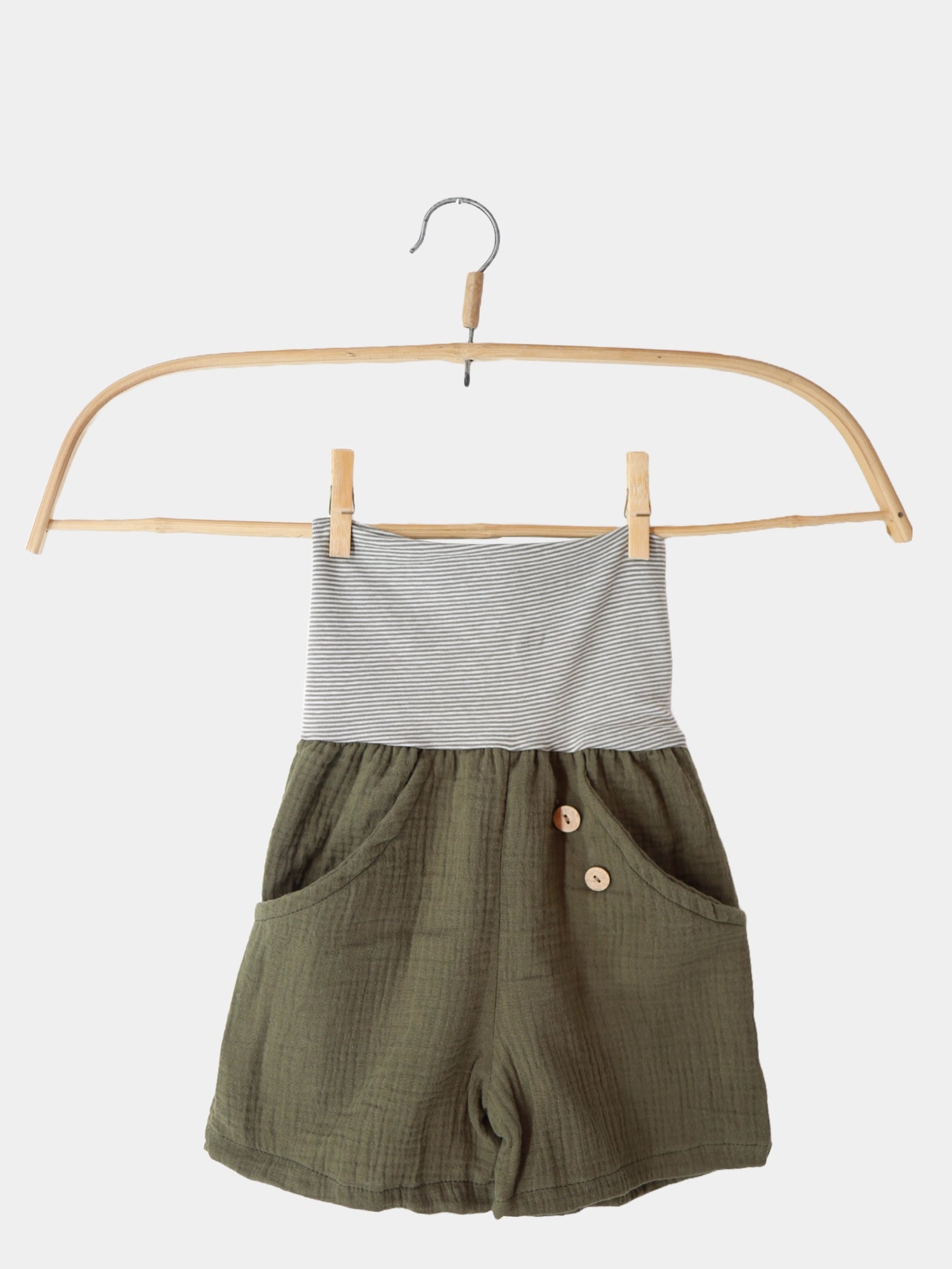 Kurze Buxe Musselin - Avocado: Ein Paar grüne Shorts mit Knöpfen auf einem Holzschwinger, gefertigt aus leichtem Musselin, ideal für den Sommer, mit einem bequemen Ringelbündchen am Bauch.