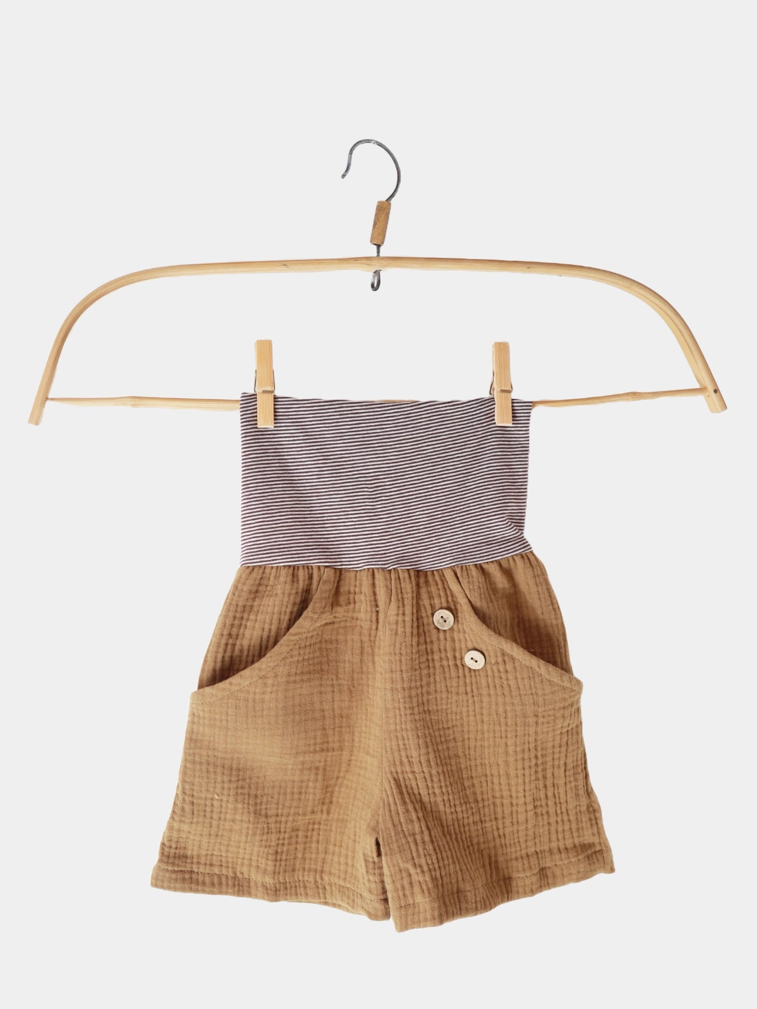 Kurze Buxe Musselin - Sahara: Braune Shorts mit Knöpfen und einem gestreiften Bund, präsentiert auf einem Holzschwinger. Leicht anzuziehen, bequem, aus Musselin-Baumwolle, ideal für den Sommer.
