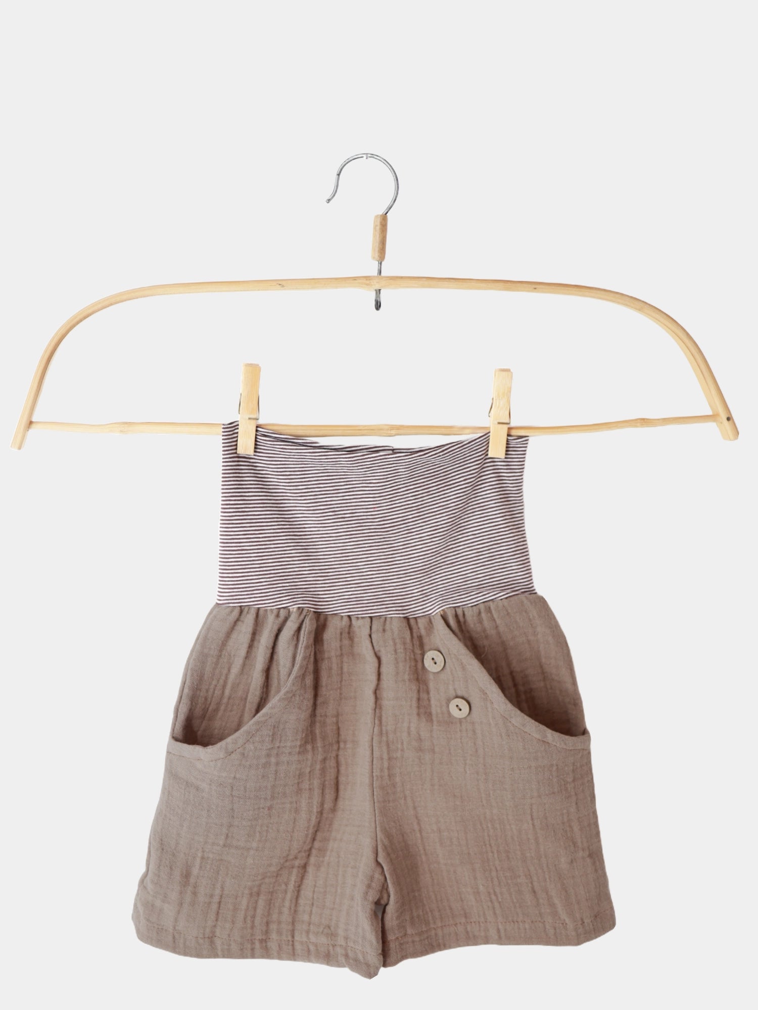 Kurze Buxe Musselin - Schlamm auf einem Holzbügel. Die Shorts mit Ringelbündchen sind aus luftigem Musselin, ideal für den Sommer, und nachhaltig in Berlin gefertigt.