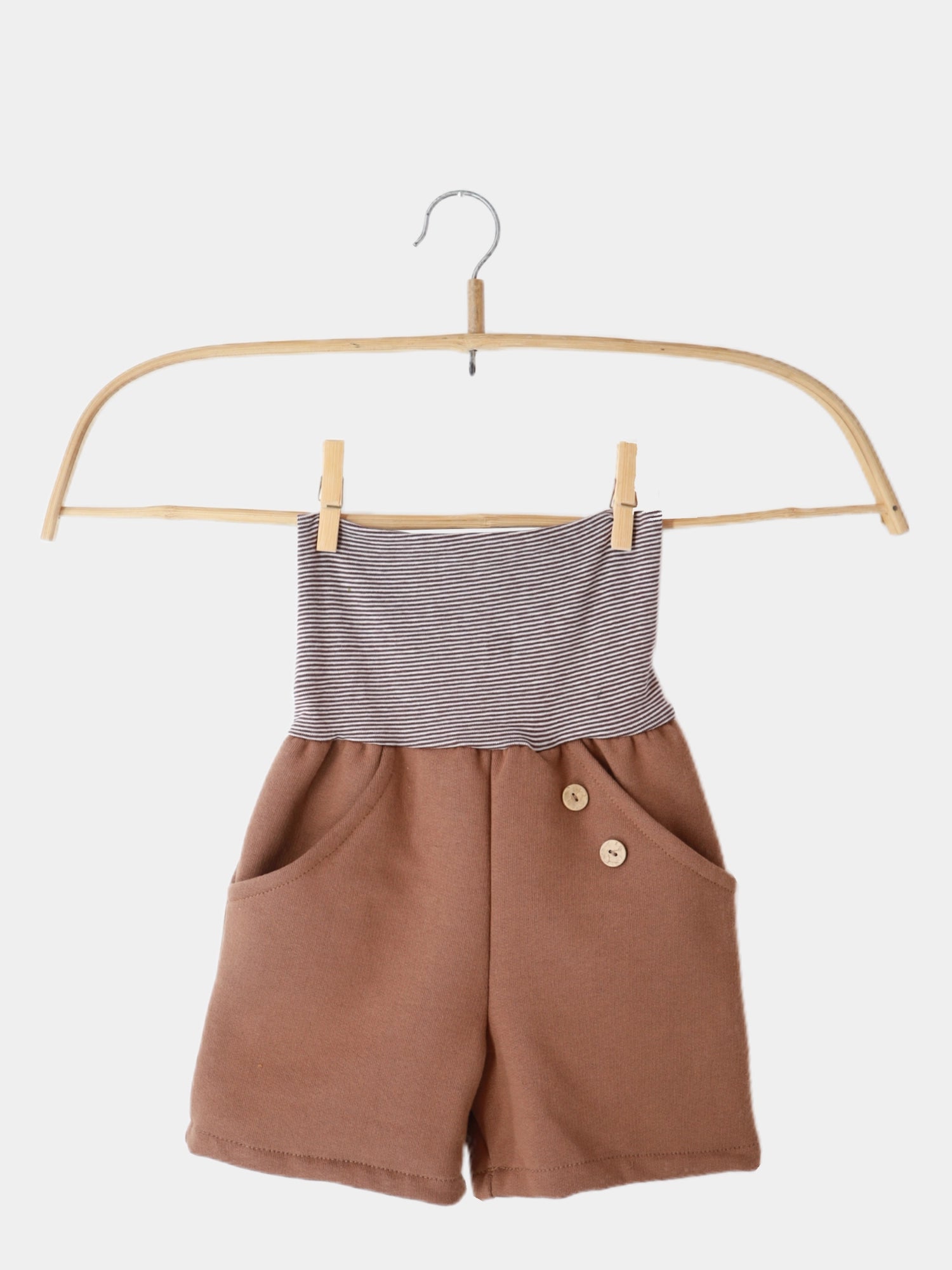 Kurze Buxe Bio-Sweat- Nougat auf einem Holzschaukel präsentiert. Die gestreiften Shorts mit Ringelbündchen sind aus weichem, nachhaltigem Baumwoll-Sweat gefertigt, ideal für den Sommer und einfach anzuziehen.