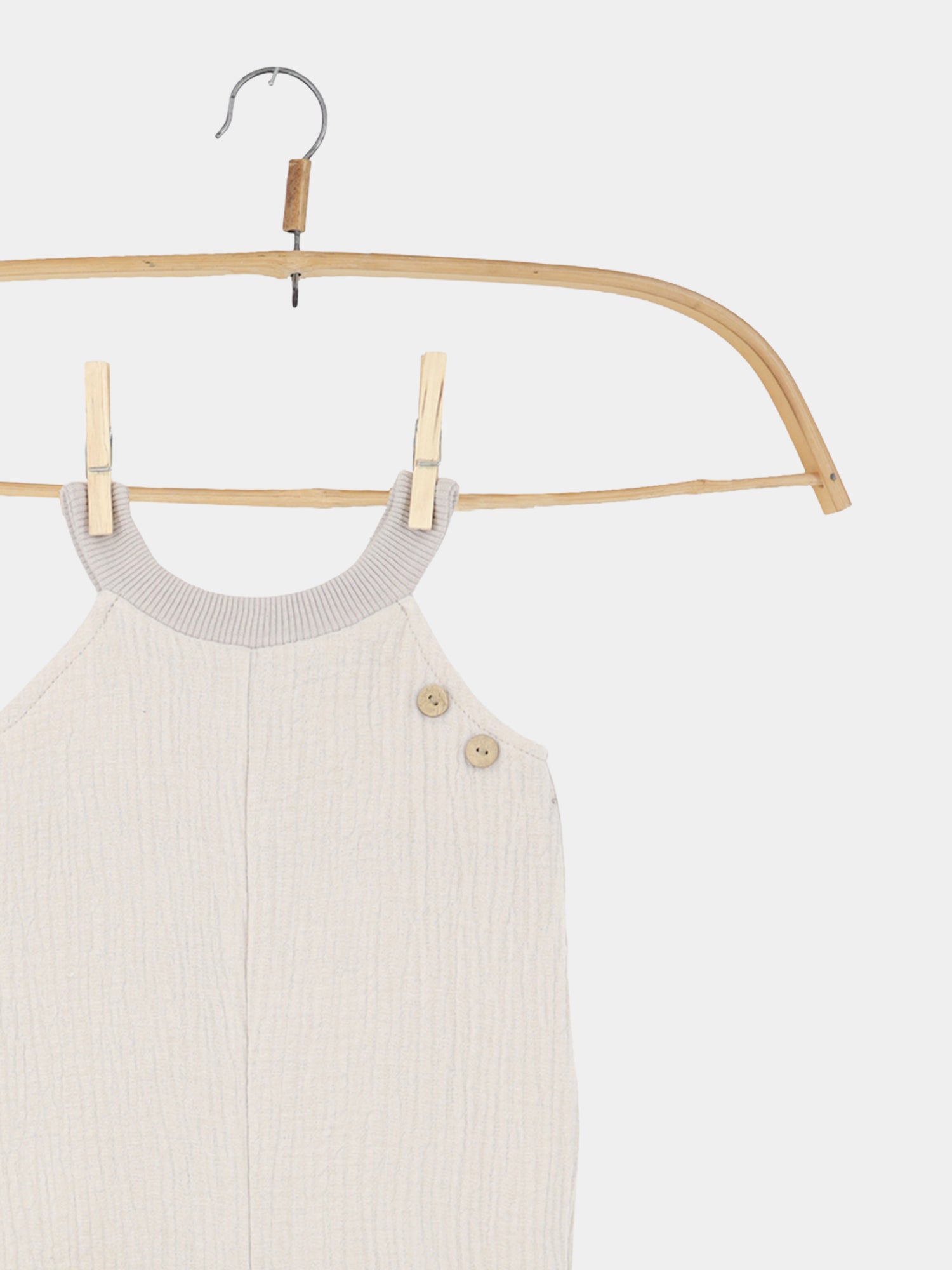 Kurze Schlupflatzhose Musselin - Sand: Ein ärmelloser Baby-Strampler aus strukturiertem Bio-Musselin, aufgehängt an einem Holzkleiderbügel mit kleinen Holzknöpfen an der Schulter, ideal für sommerliche Bewegungsfreiheit.
