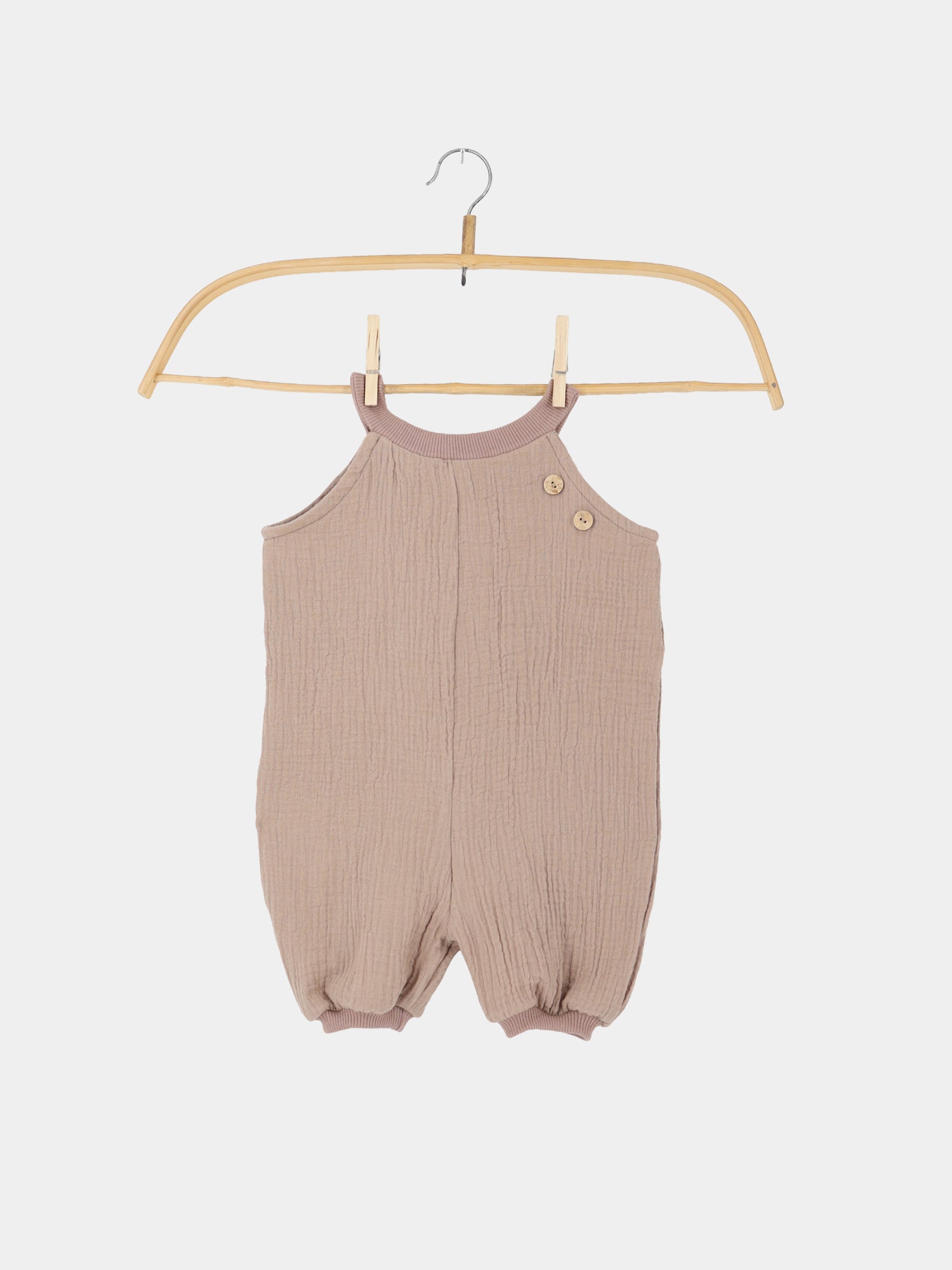 Kurze Schlupflatzhose Musselin - Milchkaffee: Ein ärmelloser Babyromper aus weichem, gekräuseltem Musselin mit Rundhalsausschnitt, Knopfverschluss an der Schulter und elastischen Beinöffnungen, auf einem Holzkleiderbügel präsentiert.