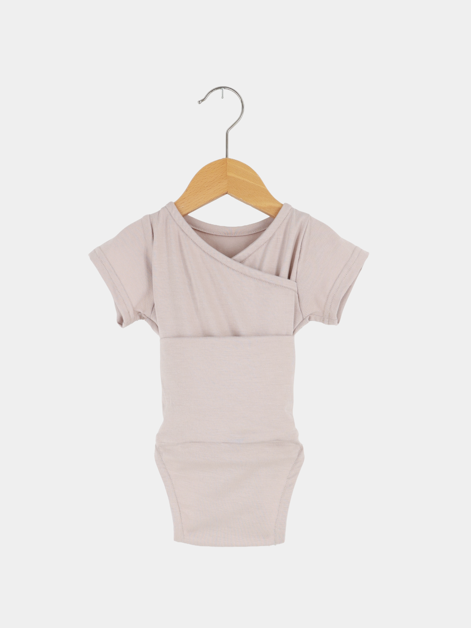 Loopbody Kurzarm Bambusviskose - Cremepuder: Ein leichter, kurzärmeliger Babybody mit kimono-artigem Vorderteil, hängend an einem Holzkleiderbügel. Ideal für den Sommer, aus weichem, temperaturausgleichendem Bambusstoff.