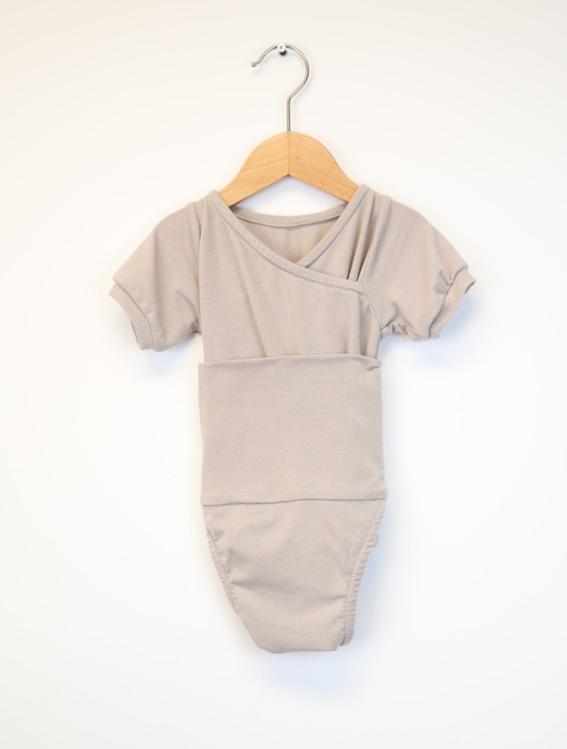 Kurzarm Loopbody Kaschmir Stein Gr. 0M: Ein einfacher, kurzärmeliger Babybody aus Kaschmir, der an einem Holzbügel hängt.