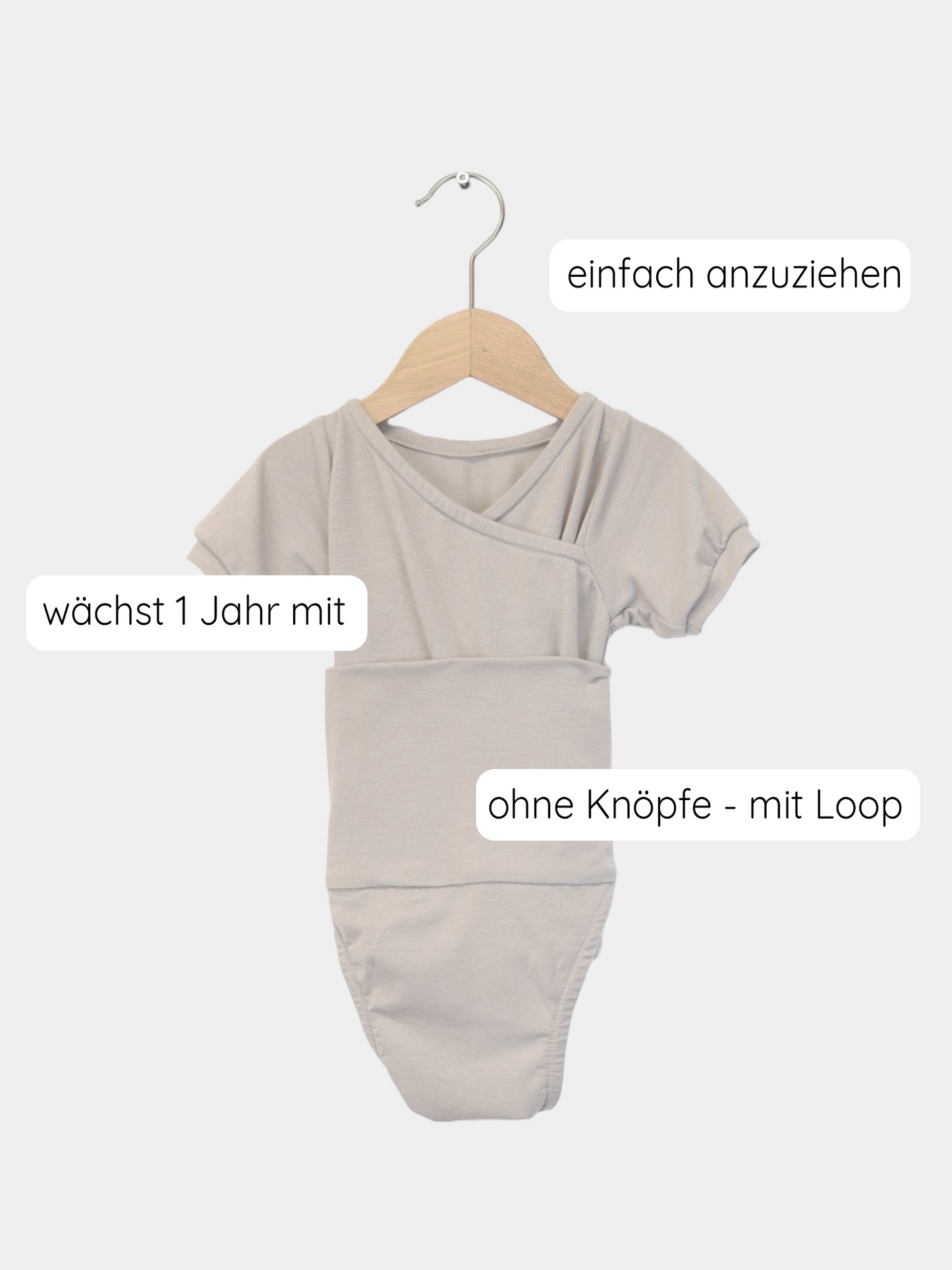 Kurzarm Loopbody Kaschmir-Mix – Sand auf einem Holzschwinger, betont durch weichen Stoff und einzigartiges Design, das sich dem Baby anpasst und leichtes An- und Ausziehen ermöglicht.