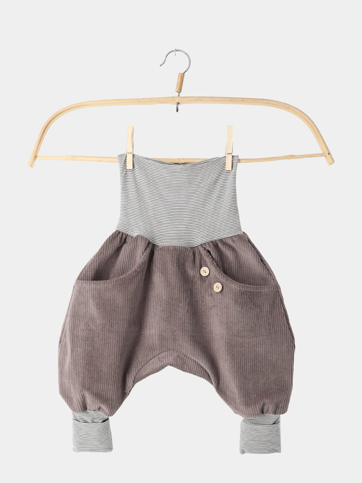 Knickerbocker Breitcord mit Ringelbündchen - Praline: Harem-Style Babyhose aus robustem, schokoladenbraunem Cord mit grauen Streifenbündchen, zwei vorderen Taschen und dekorativen Knöpfen, aufgehängt an einem Holzkleiderbügel.