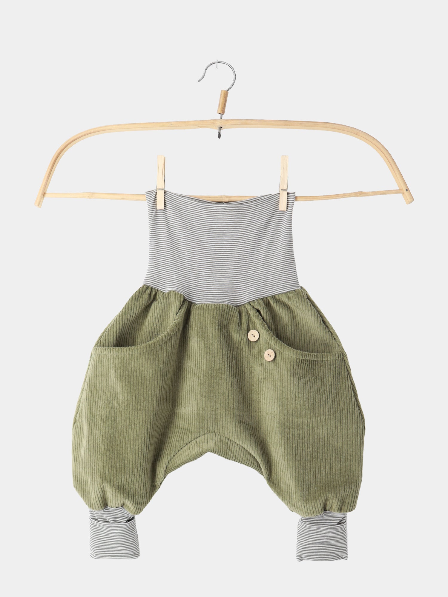 Knickerbocker Breitcord Stretch mit Ringelbündchen - Kiwi: Ein olivegrüner Cord-Romper mit gestreiftem Bund und Knöchelbündchen, zwei vorderen Taschen mit Holzknöpfen, hängend an einem Holzkleiderbügel.