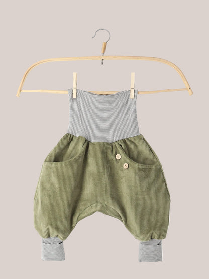 Knickerbocker Breitcord Stretch mit Ringelbündchen - Kiwi: Ein olivegrüner Cord-Romper mit gestreiftem Bund und Knöchelbündchen, zwei vorderen Taschen mit Holzknöpfen, hängend an einem Holzkleiderbügel.