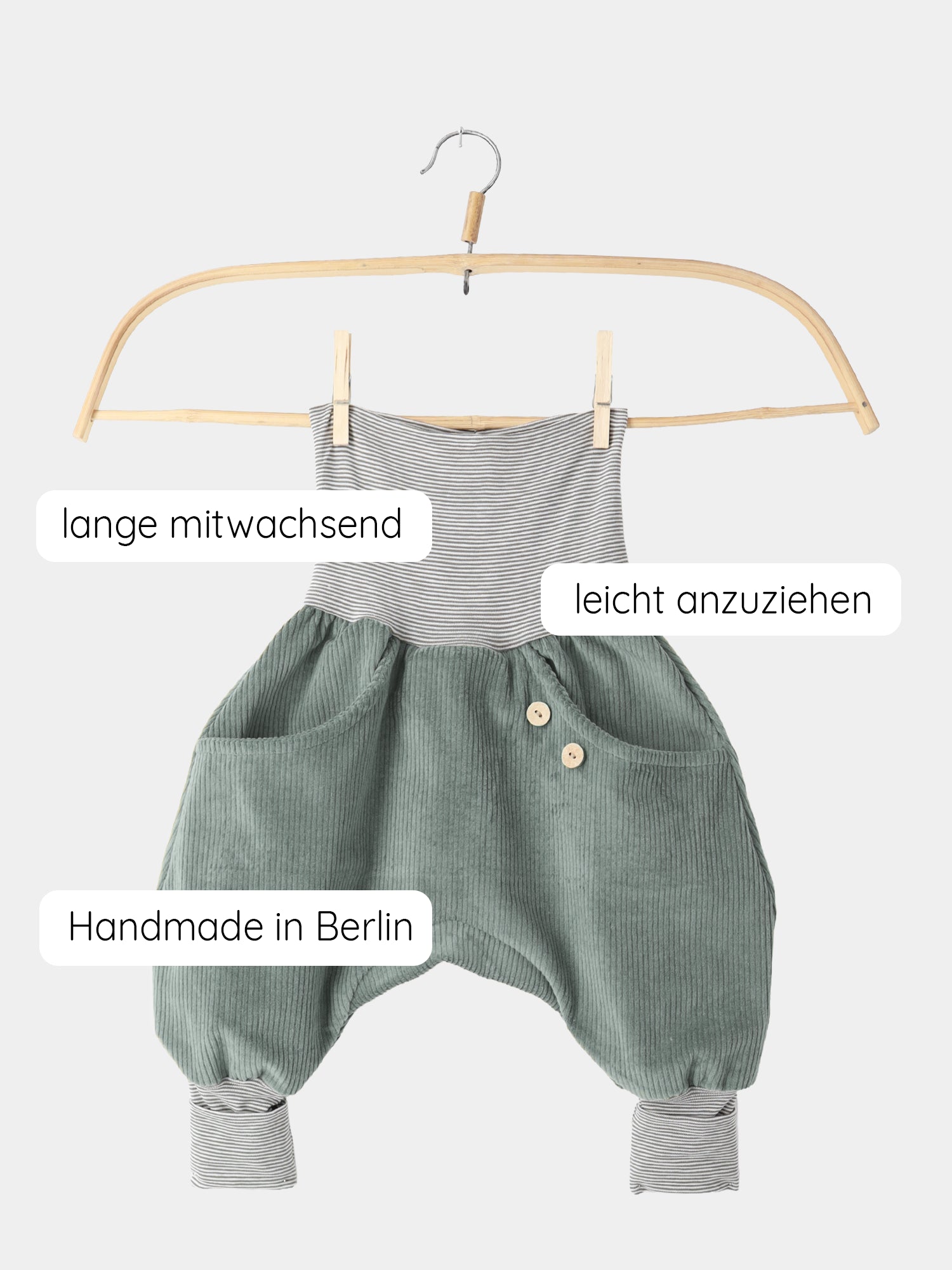 Knickerbocker Breitcord Stretch mit Ringelbündchen - Aqua: Kinder-Jumpsuit aus weichem, grünem Cordstoff mit gestreiftem Jerseybund, auf Holzkleiderbügel hängend. Handgefertigt in Berlin, mitwachsend, leicht anzuziehen.