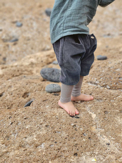 Kleines Kind trägt Knickerbocker Feincord Ringel - Blaubeere, graue Cordshorts mit gestreiftem Bund, auf sandigem Boden stehend, zeigt Bewegungsfreiheit und Komfort für aktive Entdecker:innen.