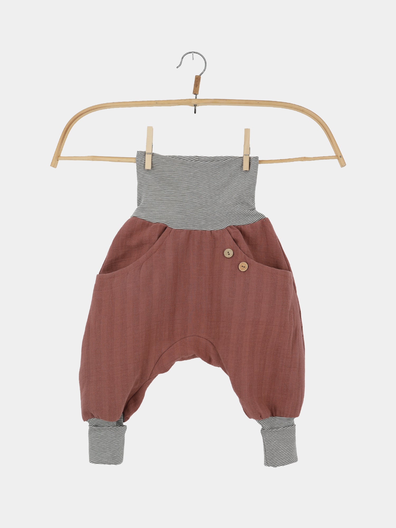 Knickerbocker Musselin aus 100% Bio-Baumwolle - Zimt: Haremshose für Kleinkinder mit breitem Bund und Knöchelbündchen, lockerer Schnitt in Terrakotta mit Vordertaschen und dekorativen Holzknöpfen auf einem Holzbügel.
