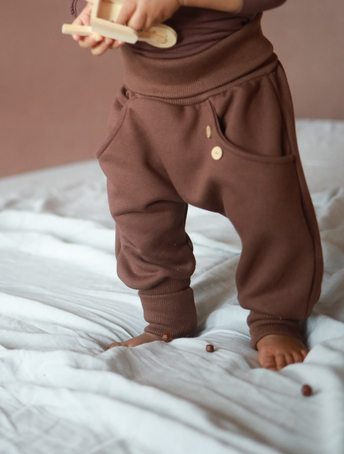 Kleinkind mit Knickerbocker Bio-Sweat - Schoko: weiche, schokoladenbraune Hosen mit tiefem Schritt, elastischen Bündchen und seitlicher Tasche mit Holzknöpfen, ideal für Spiel und Alltag.