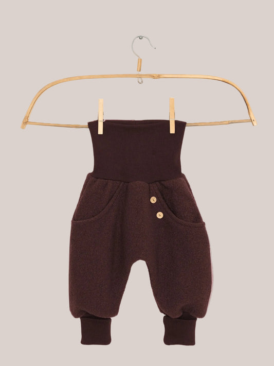 Knickerbocker boiled-wool pants – Chocolate: Small harem-style pants with a high ribbed waistband, side pockets with wooden buttons, soft wool fabric, and ribbed ankle cuffs, hanging on a wooden clothes hanger.