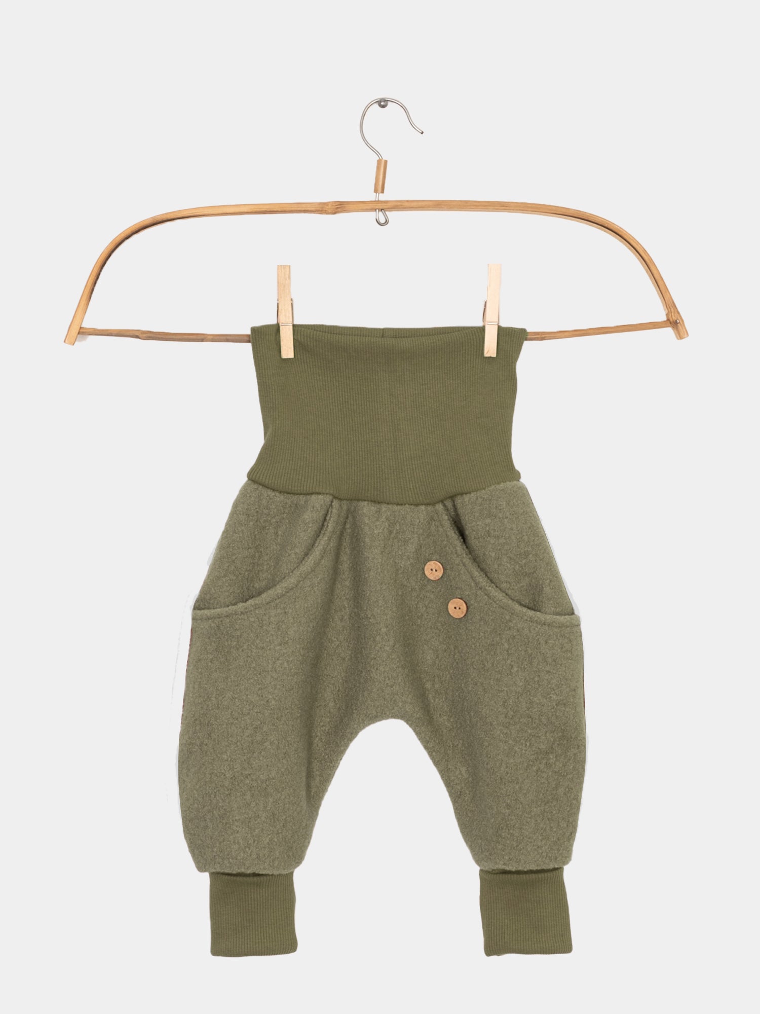 Knickerbocker Wollwalk - Pistazie: Grün gestrickte Baby-Latzhose auf Bügel. Mit Knöpfen und Kängurutaschen, ideal für kaltes Wetter. Perfekt für Jungen und Mädchen, handgefertigt in Berlin.