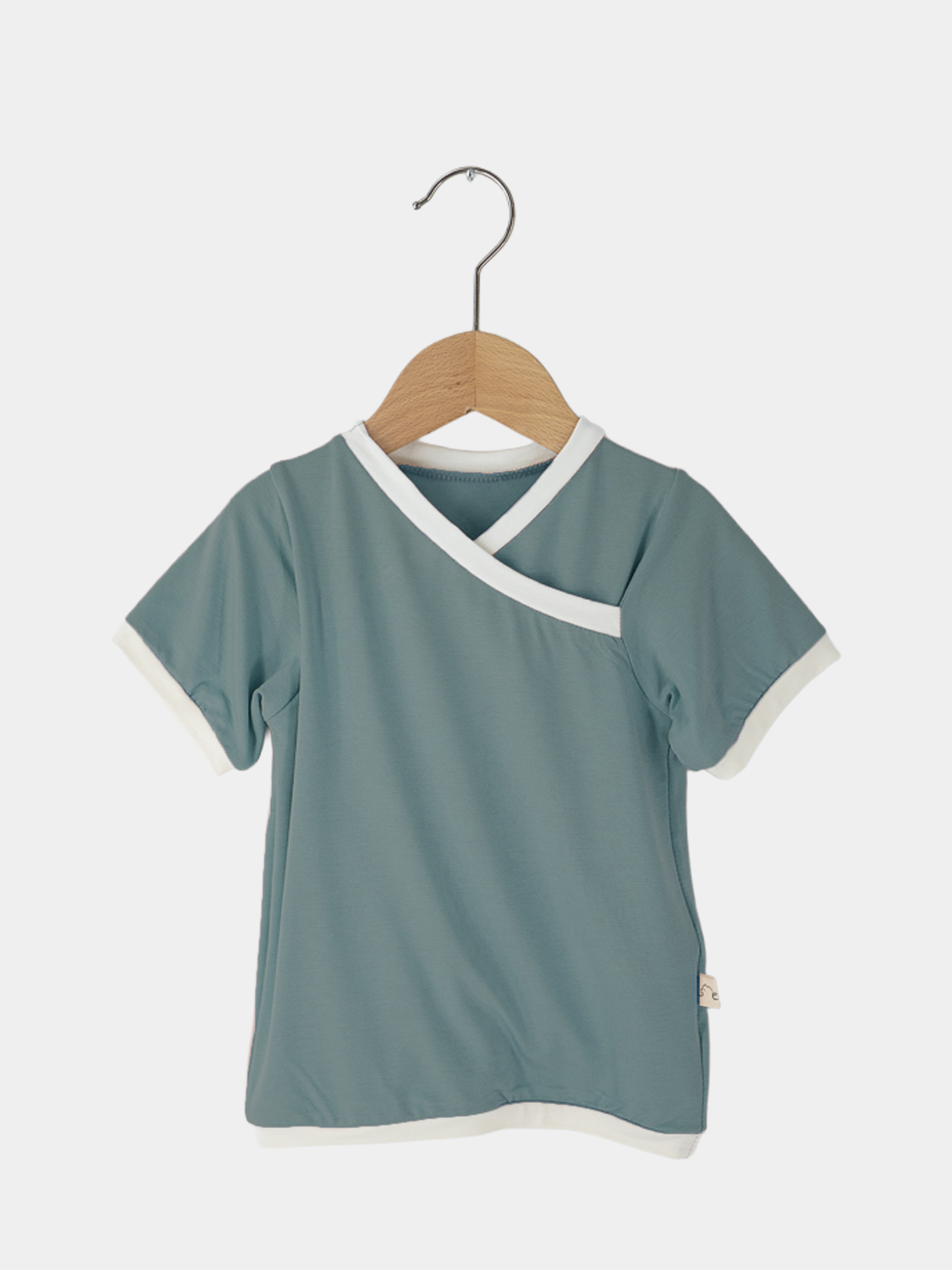 Kurzes Wickelshirt Bambusviskose - Türkis auf einem Holzkleiderbügel, zeigt den lässigen Schnitt und die Wickeloptik. Ideal für Sommer, antibakteriell und schnell trocknend, perfekt für Kinder von 2-3 Jahren.