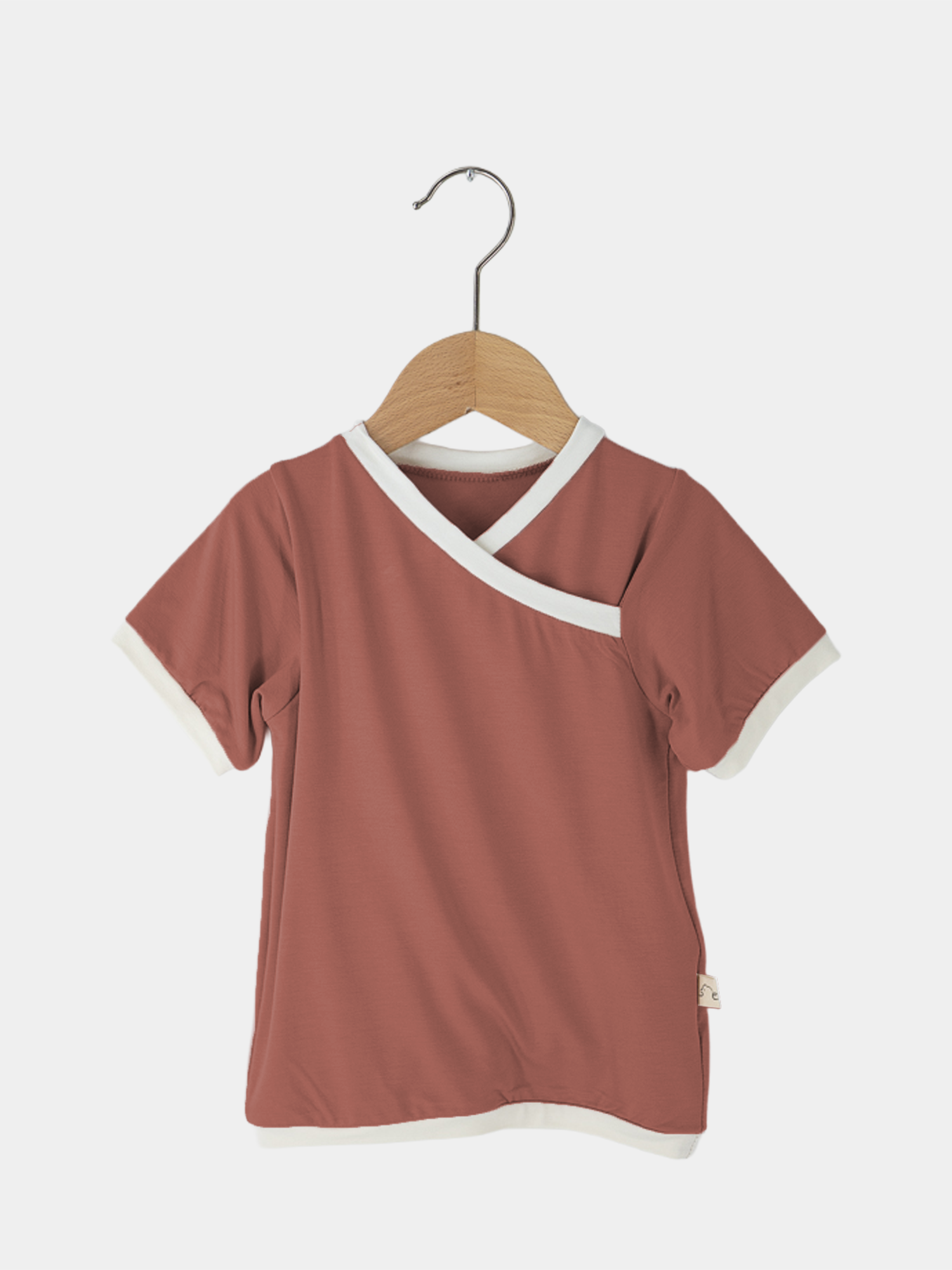 Kurzes Wickelshirt Bambusviskose - Pfirsich auf einem Kleiderbügel, zeigt den Wickelausschnitt und die kurzen Ärmel. Handgenäht, ideal für Kinder von 2-3 Jahren, passend für Sommeraktivitäten.
