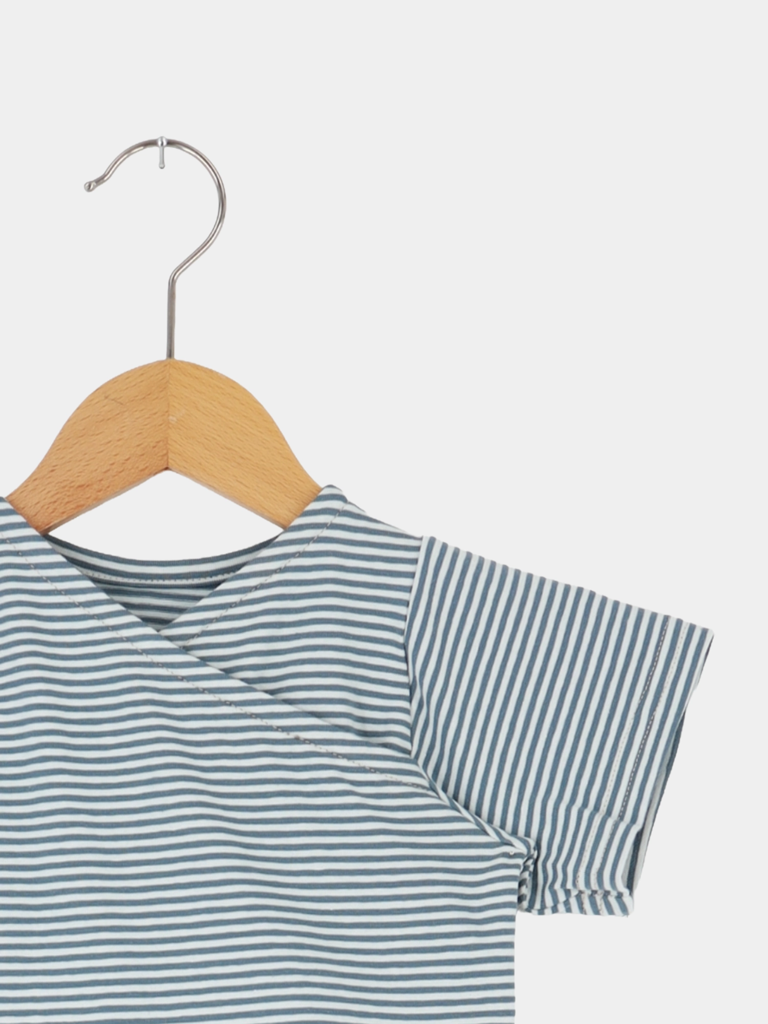 Kurzes Wickelshirt Baumwolle - Ringel Taube hängt auf einfachem Holzbügel, zeigt feine blau-weiße Streifen und einen kimonoartigen Wickelausschnitt, ideal für sommerliche Outfits, handgefertigt in Berlin.