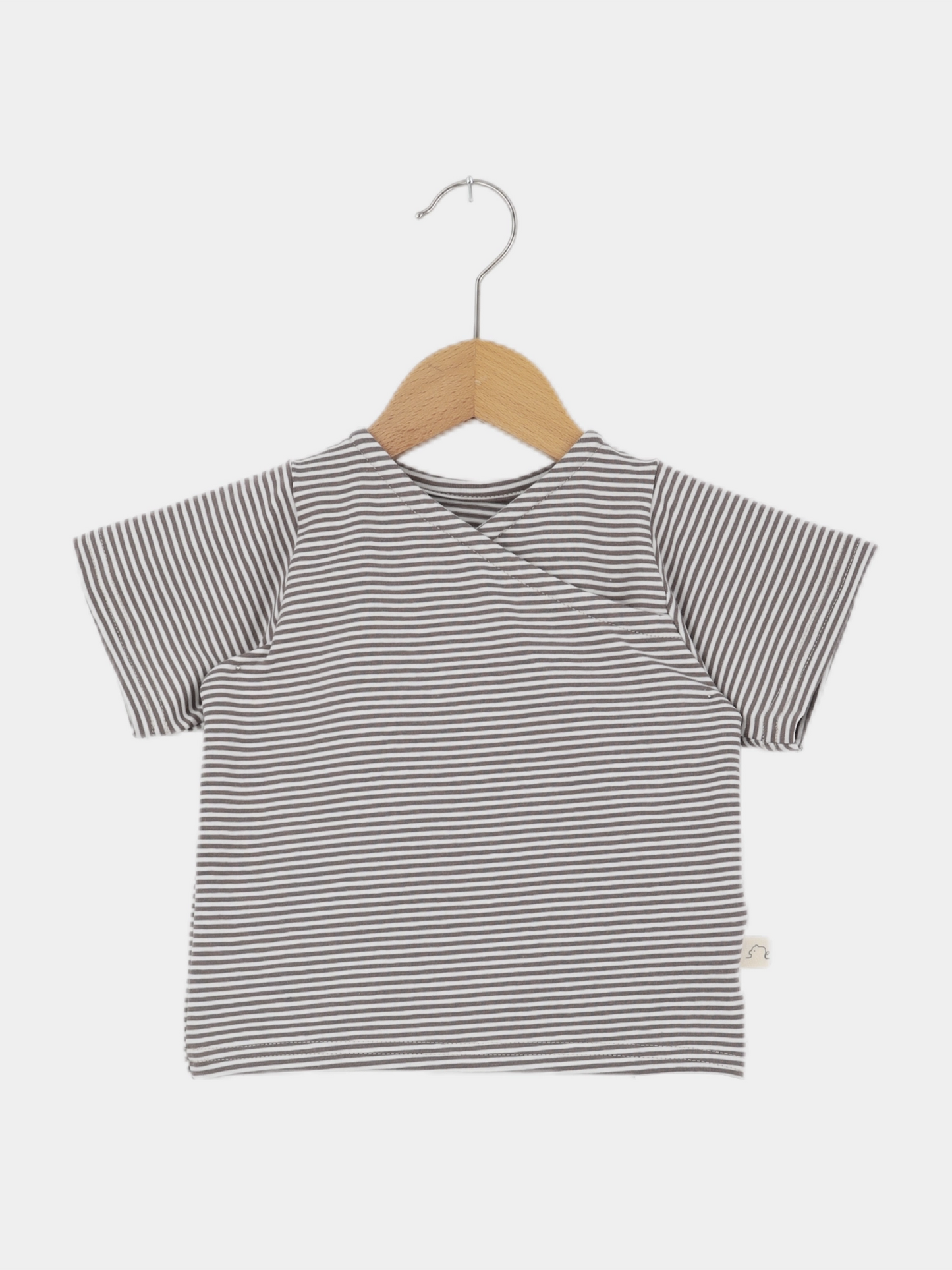 Kurzes Wickelshirt Baumwolle - Ringel Praline: Kurzärmeliges Shirt mit schmalen grauen und weißen Streifen, präsentiert auf einem Holzkleiderbügel. Ideal für Kinder, handgefertigt in Berlin aus atmungsaktiver Baumwolle.