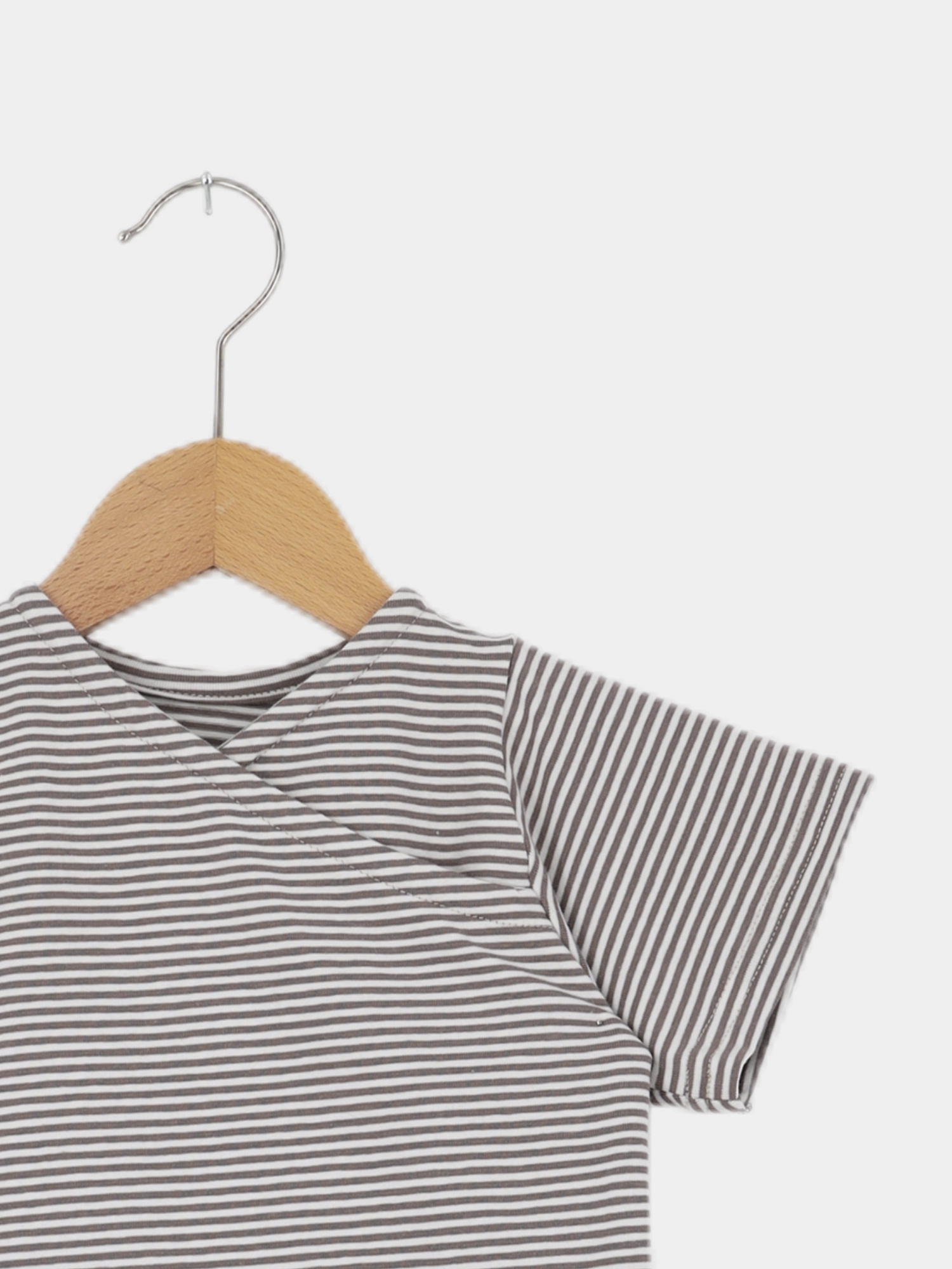 Kurzes Wickelshirt Baumwolle - Ringel Praline: Ein kurzärmeliges, grau-weiß gestreiftes Kinderoberteil auf einem Holz-Metall-Bügel, handgefertigt in Berlin, weich, bequem und aus elastischer, atmungsaktiver Ökotex-zertifizierter Baumwolle.