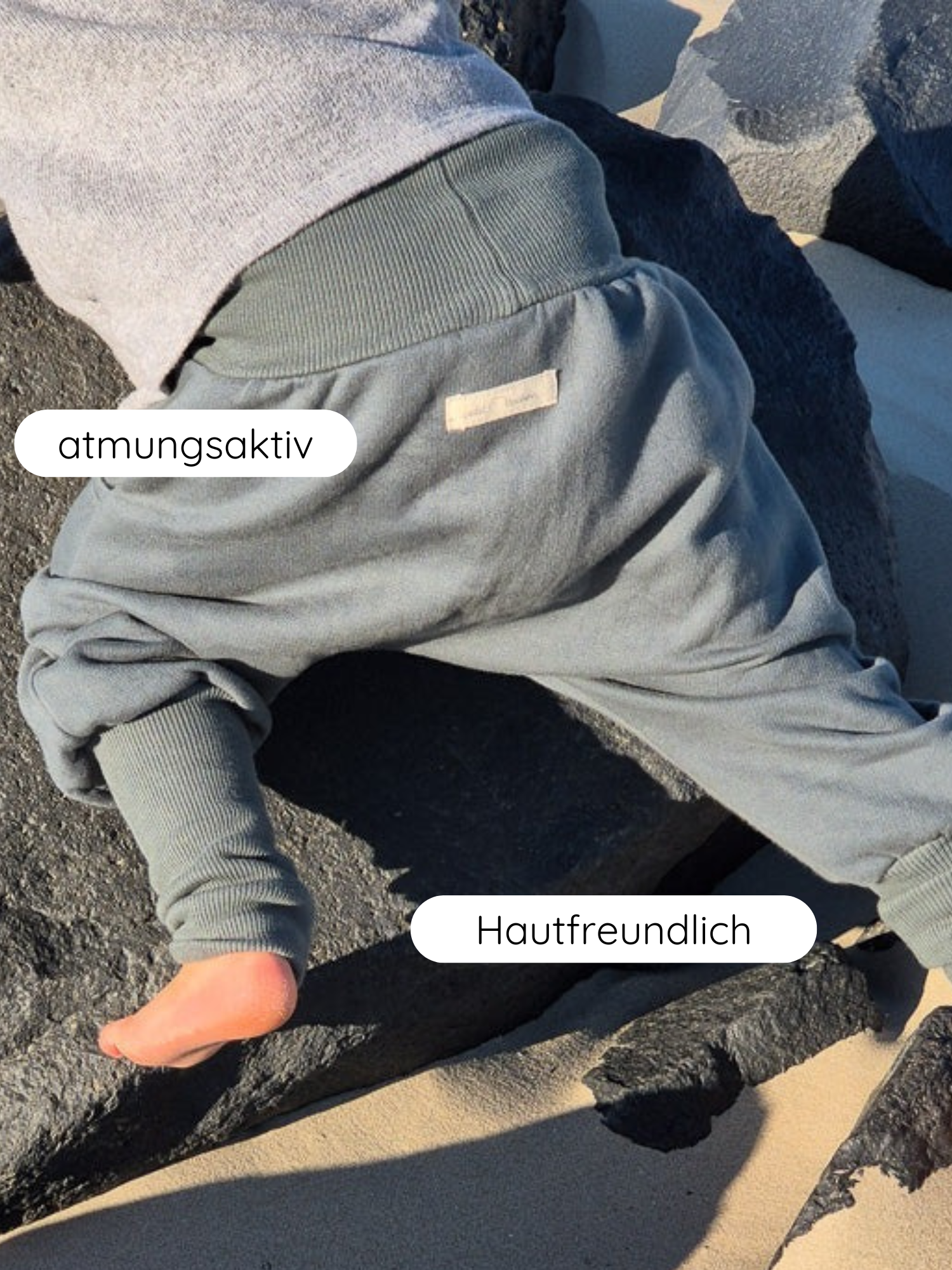 Kleinkind krabbelt auf dunklen Felsen im Knickerbocker Bio-Sweat - Taube. Die weichen, graugrünen Hosen sind atmungsaktiv und hautfreundlich, ideal für Bewegungsfreiheit und Komfort.