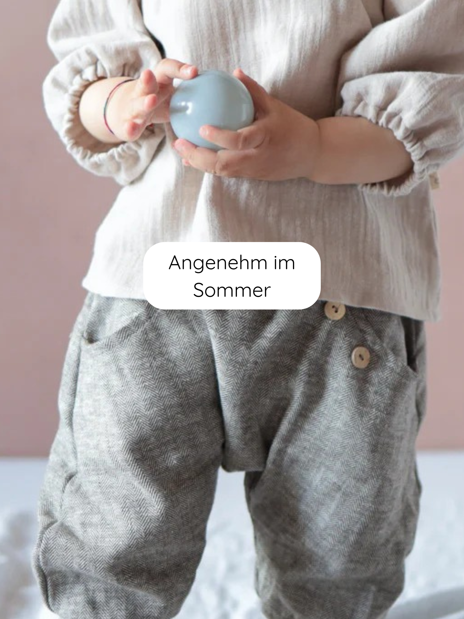 Kleinkind trägt Knickerbocker Fischgrat aus Leinen-Baumwoll-Mix, lose geschnitten mit hölzernen Bundknöpfen, hält einen pastellblauen Ball. Ideal für Komfort und Bewegungsfreiheit im Alltag.