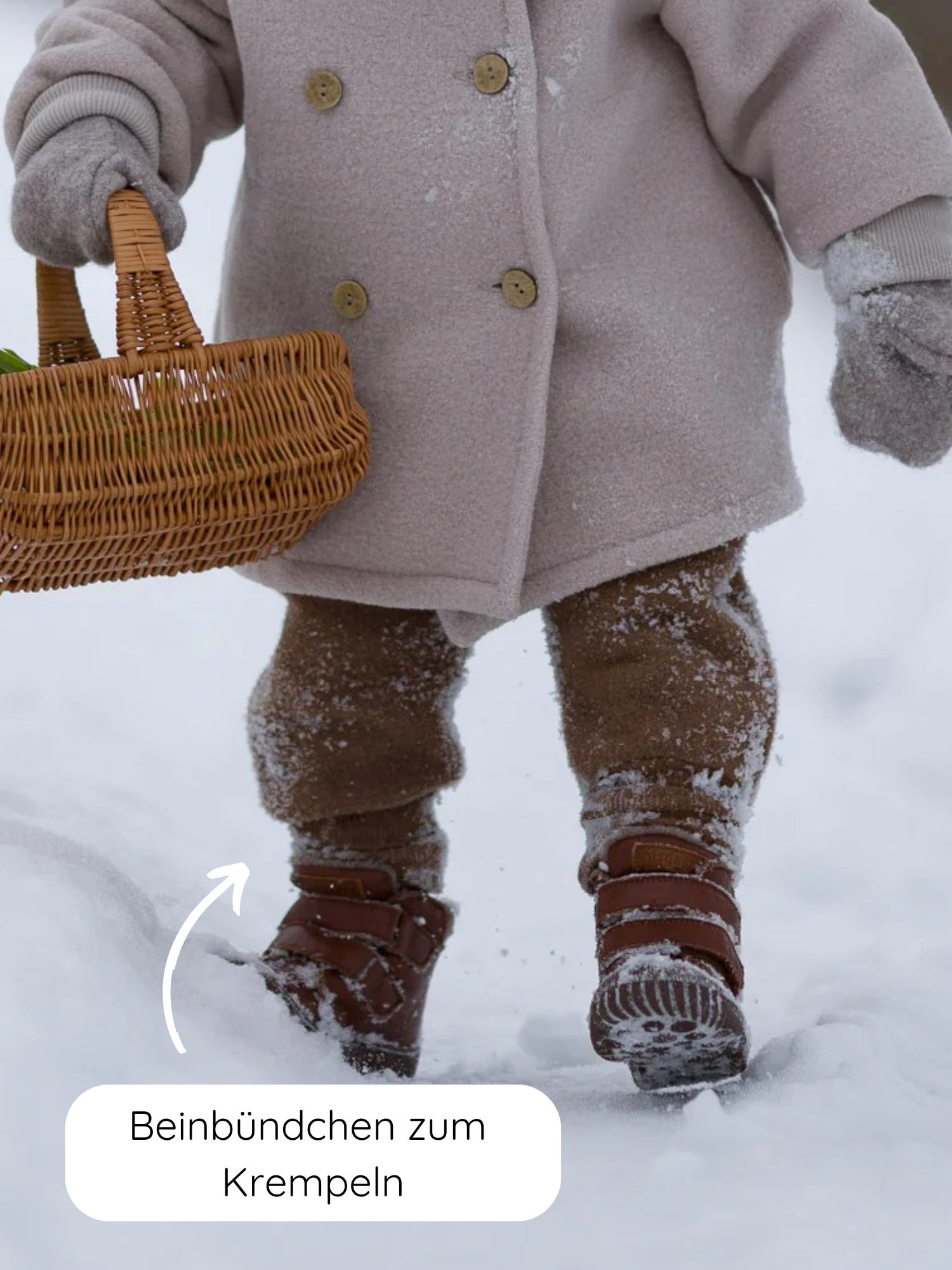 Nahaufnahme eines Kindes im Schnee mit einer Knickerbocker Wollwalk - Schoko. Die Hose hat breite krempelbare Beinbündchen, ideal für Winterstiefel, und Kängurutaschen, handgefertigt in Berlin.