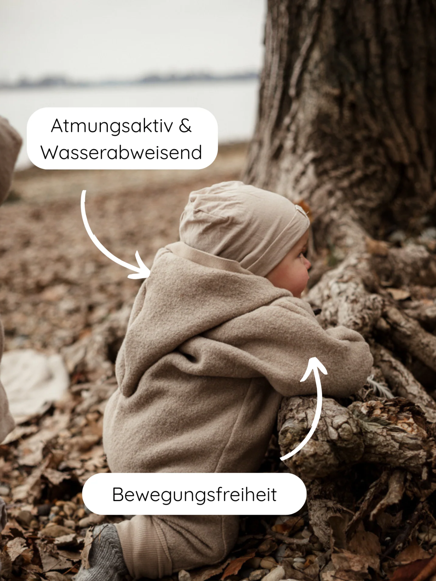 Kleinkind kniet am Seeufer in einem Kuschelanzug Wollwalk - Sand. Der Anzug zeigt Funktionen: atmungsaktiv, wasserabweisend und Bewegungsfreiheit, ideal für Outdoor-Aktivitäten.