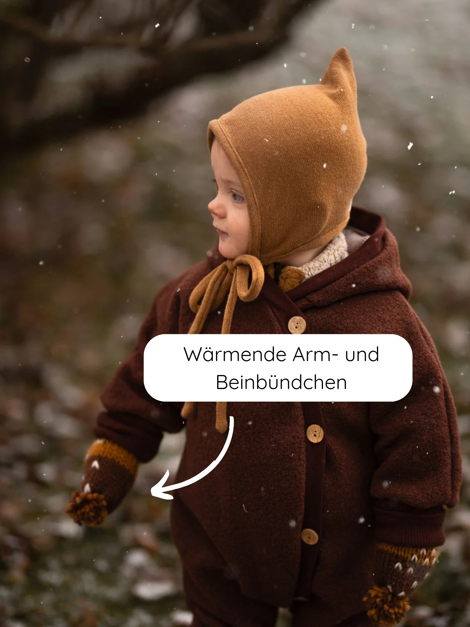 Kleinkind in winterlichem Outfit trägt den Kuschelanzug Wollwalk - Schoko: warme Arm- und Beinbündchen, Holzknöpfe, Kapuze mit Ohren, passende Mütze und Handschuhe, ideal für kalte Jahreszeiten.