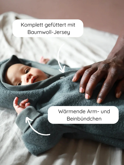 Ein Baby liegt in einem Kuschelanzug Wollwalk - Taube, vollständig mit Baumwoll-Jersey gefüttert, mit wärmenden Arm- und Beinbündchen. Eine Hand zeigt die Passform des Anzugs.