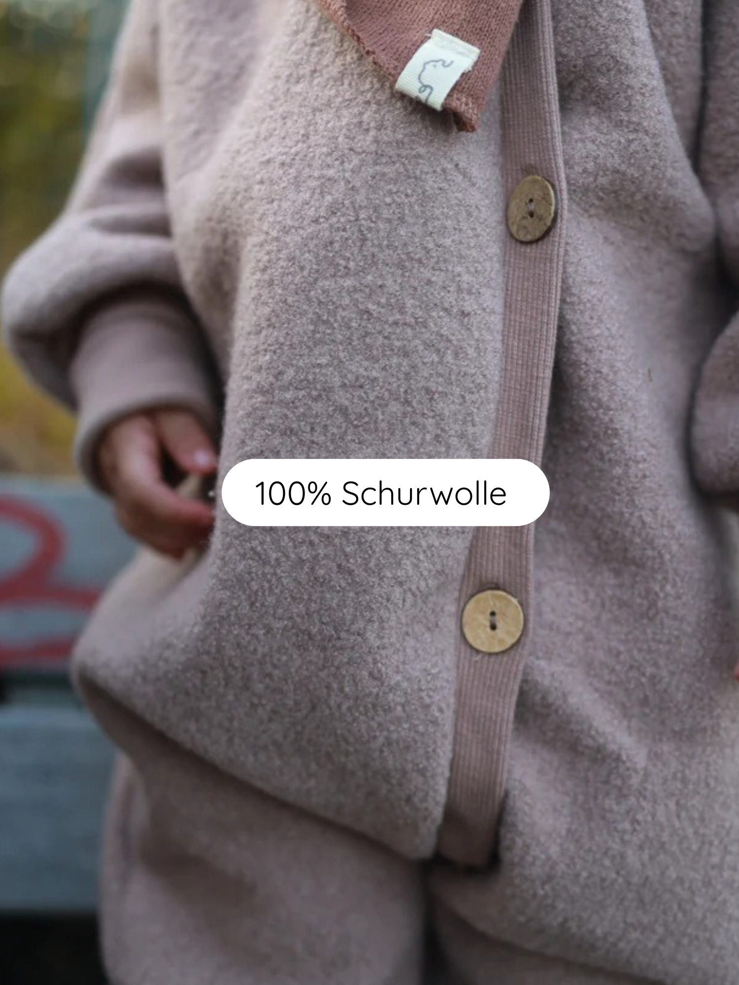 Kuschelanzug Wollwalk - Puder: Nahaufnahme eines weichen Wolloutfits mit Bouclé-Struktur, bestehend aus Jacke mit Holzknöpfen und Hose, aus 100 % Schurwolle. Ein Kinderhand sichtbar.