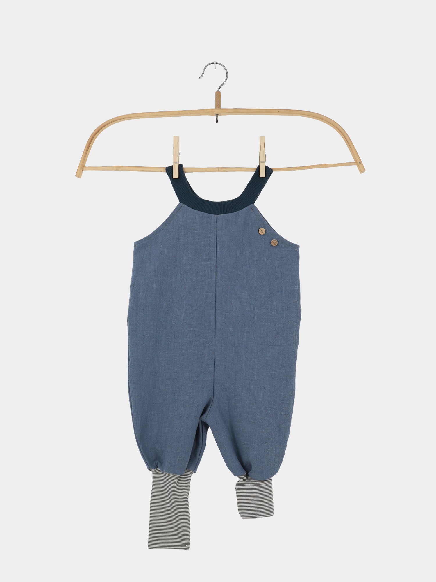 Schlupflatzhose Leinen - Blaubeere: Einteiler aus weichem Denimblau mit dunklem geripptem Halsband, Holzknöpfen auf einer Schulter, gerafften Beinen und grau-weiß gestreiften Bündchen.
