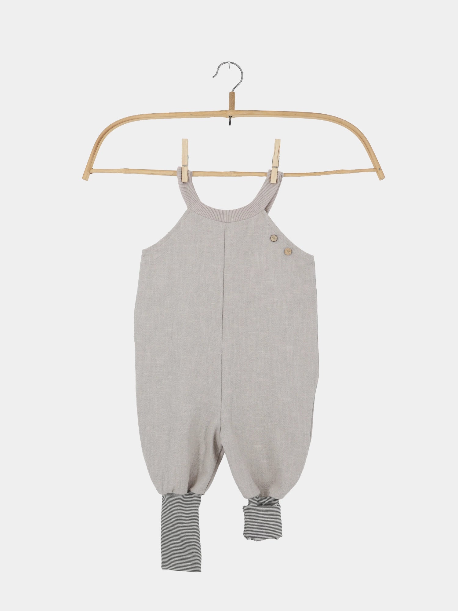Einzelstück Schlupflatzhose Leinen - Sand: Grauer ärmelloser Einteiler mit Knopfdetails an den Schultern, leicht bauschige Beine, gestreifte Bündchen am Knöchel, präsentiert an einem Holzkleiderbügel.