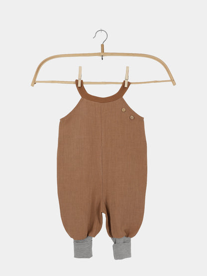 Schlupflatzhose Leinen - Weizen: Ein brauner Leinenromper für Kleinkinder mit Halterneck, Holzknöpfen und grauen gestreiften Bündchen an den Beinen, hängend an einem Holzbügel.