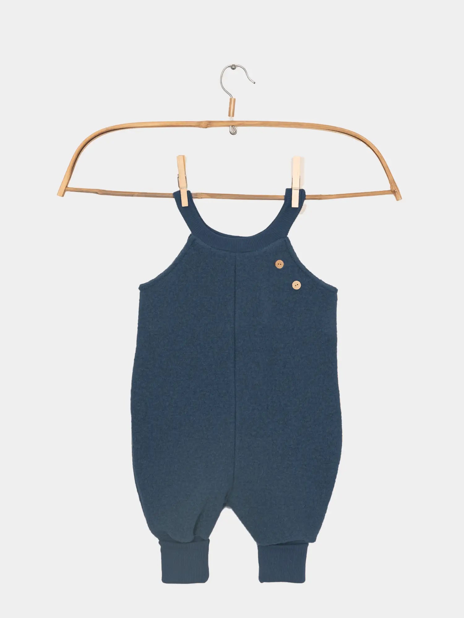 Schlupflatzhose Wollwalk aus 100% Schurwolle - Marine: Navy-blauer, ärmelloser Strampelanzug mit Rundhalsausschnitt, zwei Holzknöpfen an der Schulter und gerippten Bündchen an den Knöcheln, hängend an einem Holzkleiderbügel.
