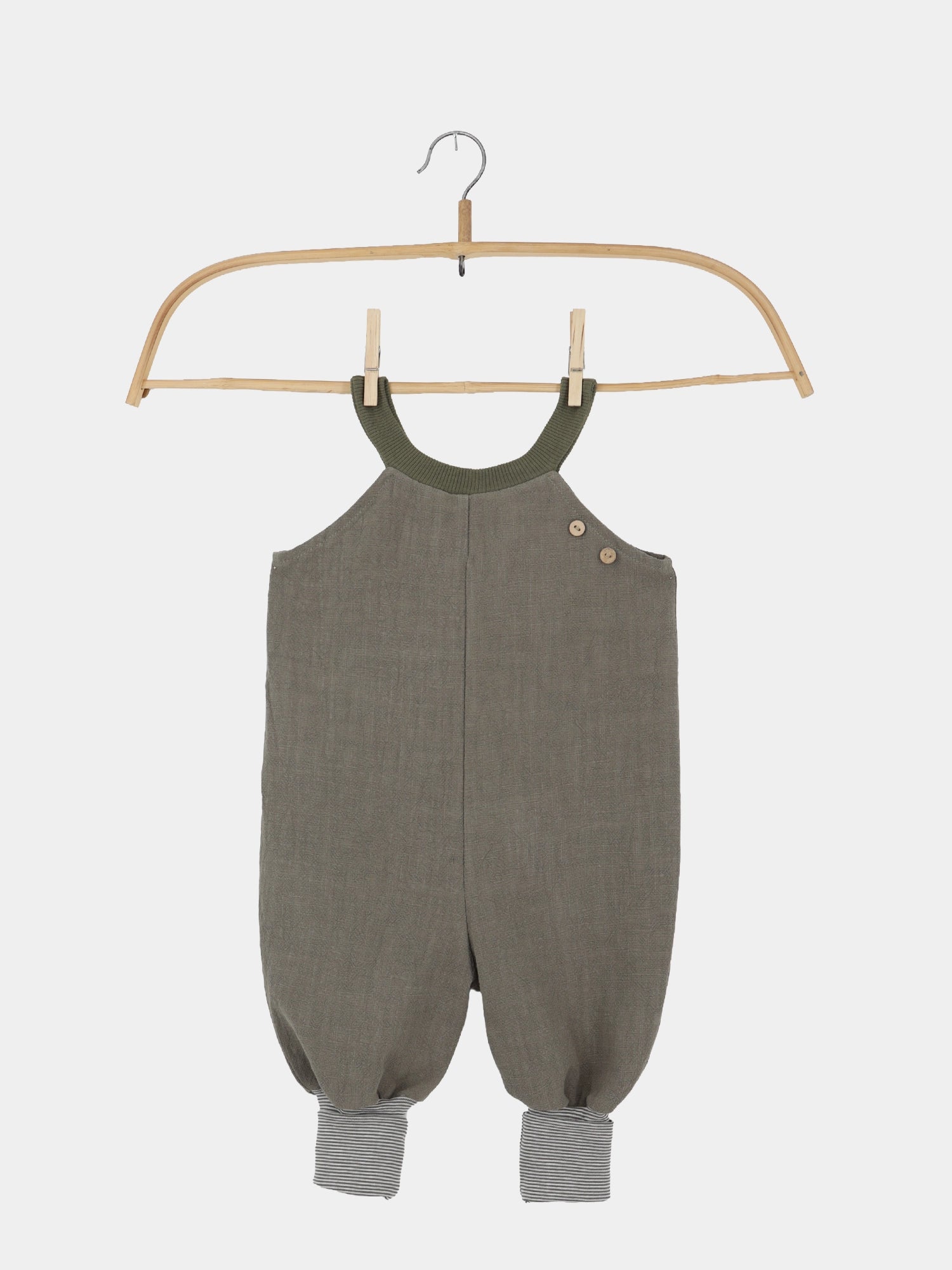 Schlupflatzhose Leinen - Oliv: Ein olivgrüner Baby-Strampler hängt an einem schmalen Holzbügel, mit Rippenbündchen, Knopfverschluss an der Schulter, ballonartigem Schnitt und gestreiften Umschlagbündchen an den Knöcheln.