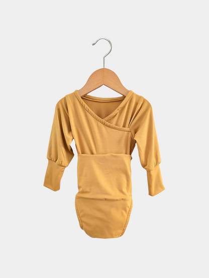 Loopbody Bambusviskose - Honig: Langärmeliger, senfgelber Babybody mit asymmetrischem Wickelausschnitt und verlängerten Bündchen, aus weichem, atmungsaktivem Bambusstoff, auf einem Holzkleiderbügel hängend.