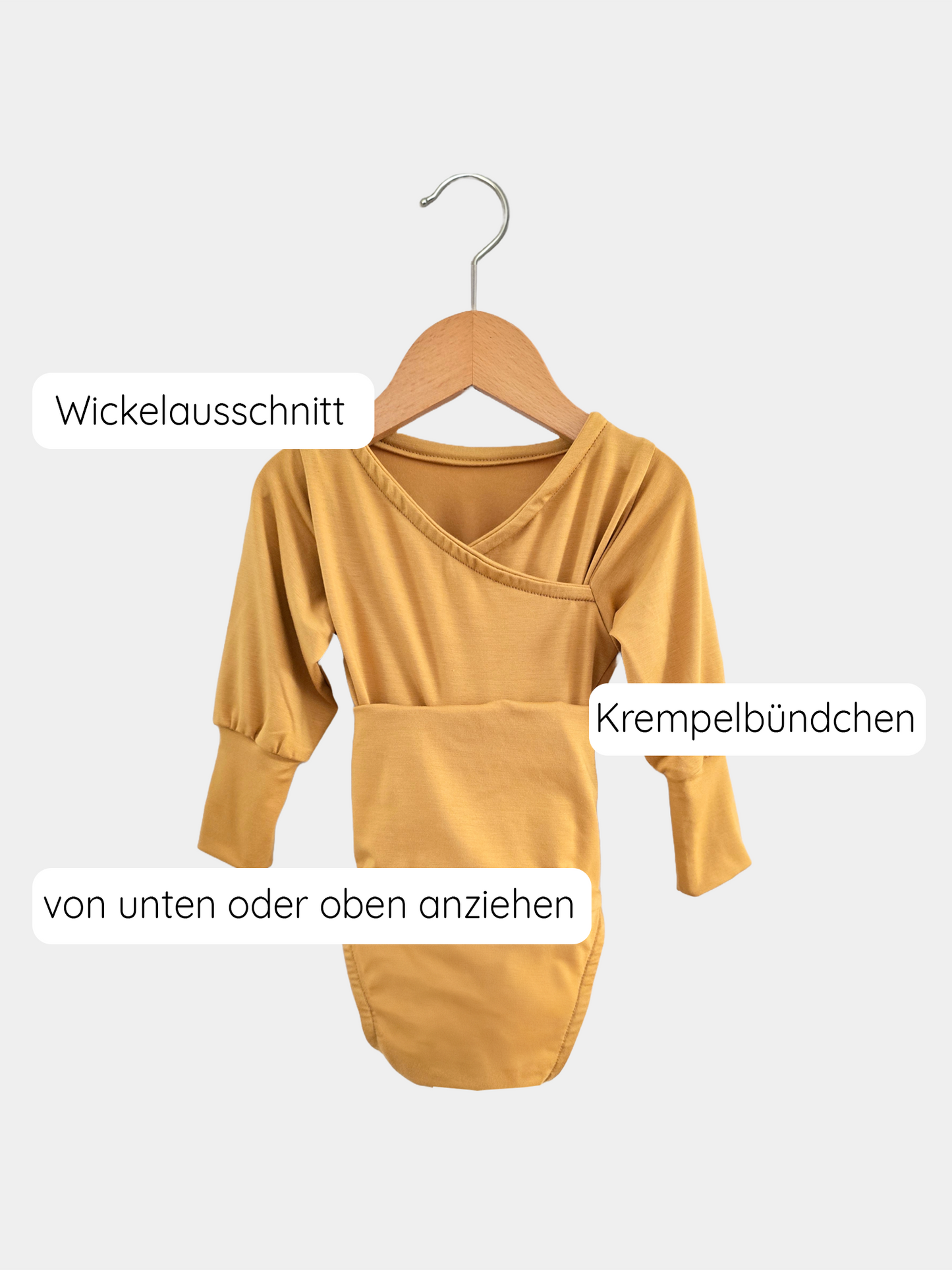 Loopbody Bambusviskose - Honig: Mustard-gelber Langarm-Babybody auf Holzbügel, Wickelausschnitt, Krempelbündchen, anziehbar von oben oder unten, bequem mitwachsend, aus weichem, atmungsaktivem und antibakteriellem Bambusstoff.