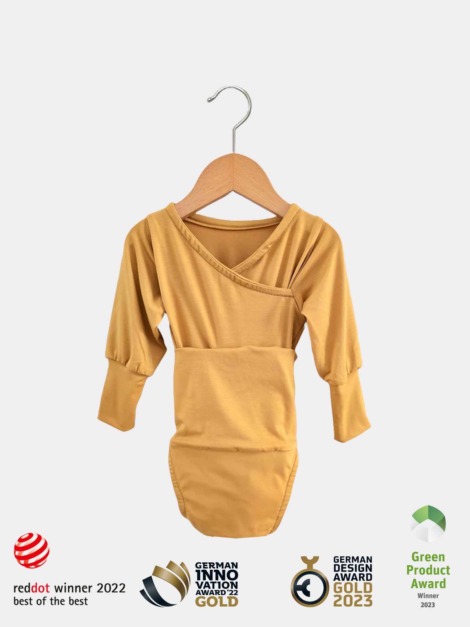 Loopbody Bambusviskose - Honig: Ein langärmliger, wickelbarer Babybody in senfgelb aus weicher Bambusviskose, auf einem Holzbügel hängend. Prämiert mit vier renommierten Design- und Innovationspreisen.