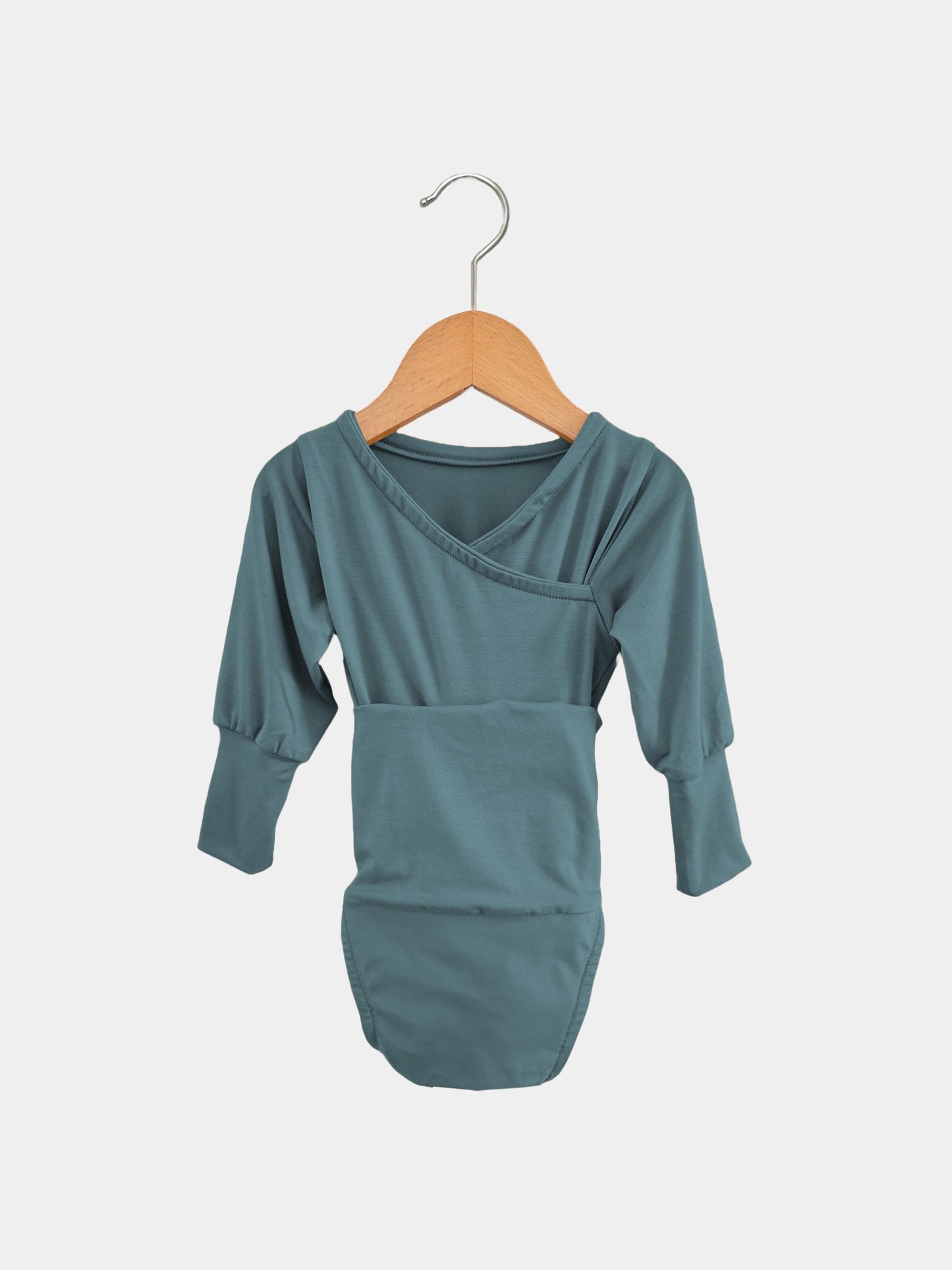 Der Loopbody Bambusviskose - Ozean zeigt einen langärmeligen, mitwachsenden Babybody in gedecktem Türkis mit Umschlaghals. Er hängt an einem Holzkleiderbügel vor einem schlichten Hintergrund.