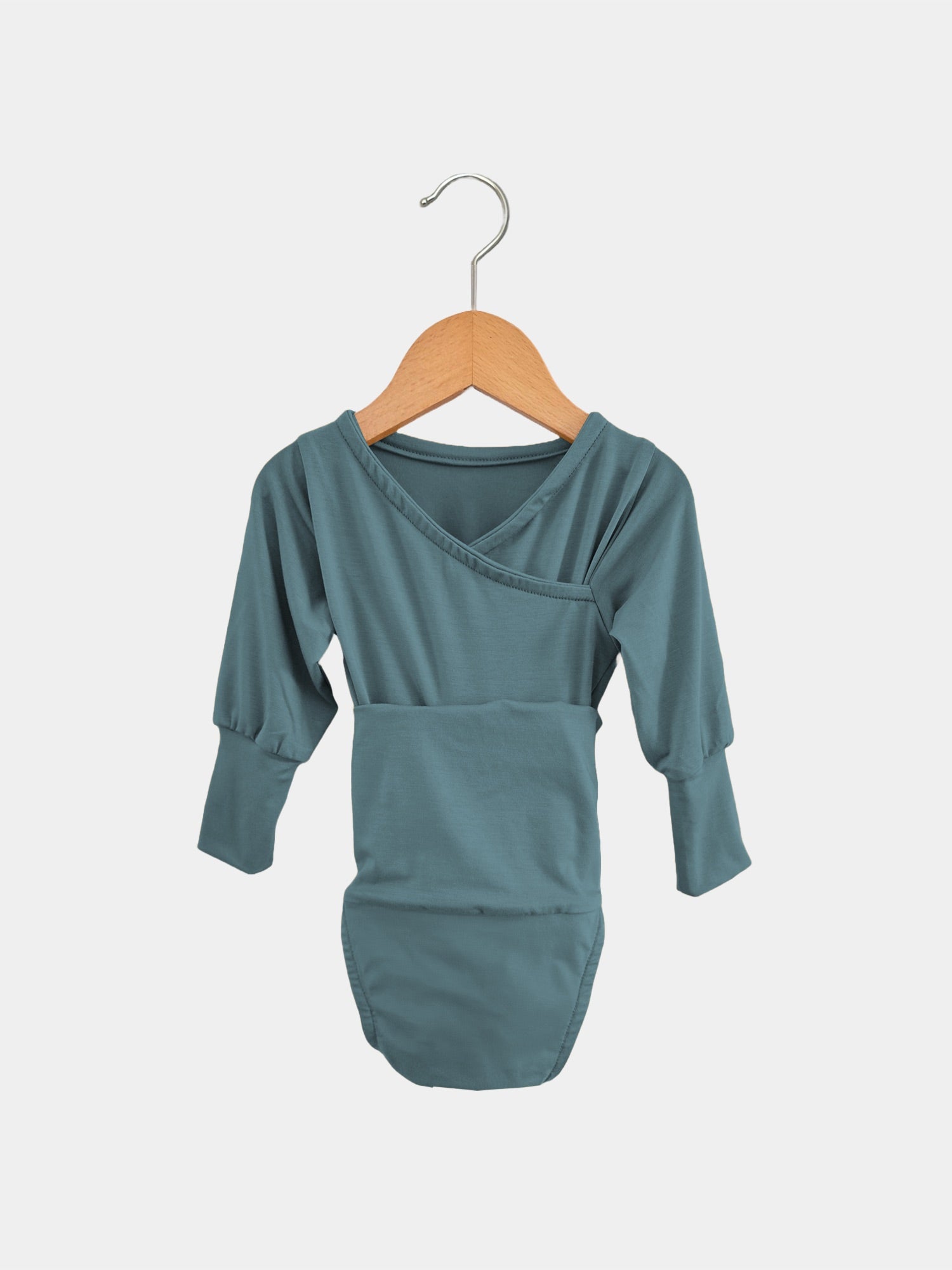 Der Loopbody Bambusviskose - Ozean zeigt einen langärmeligen, mitwachsenden Babybody in gedecktem Türkis mit Umschlaghals. Er hängt an einem Holzkleiderbügel vor einem schlichten Hintergrund.
