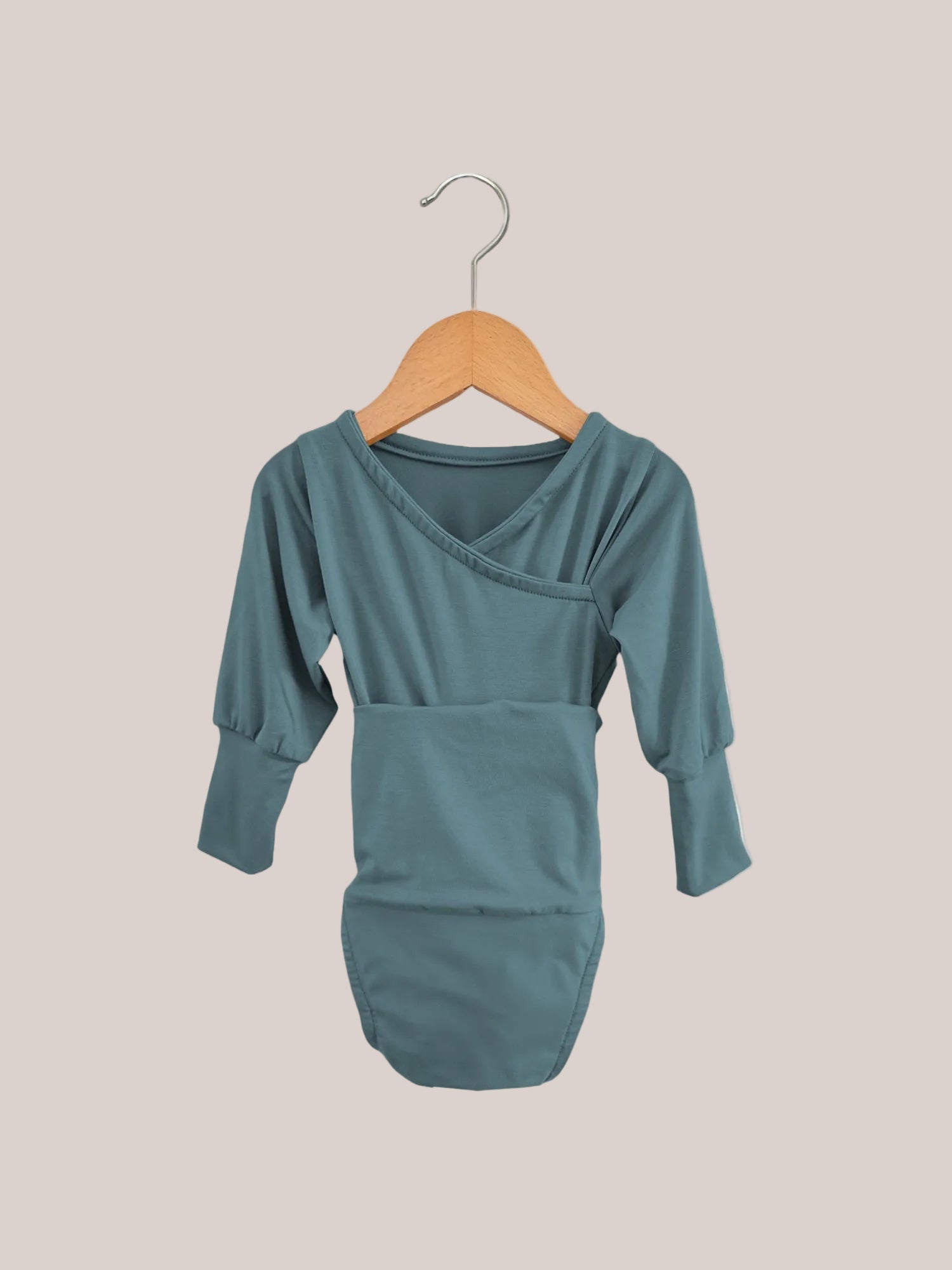The Loopbody Bamboo Viscose – Ocean features a long-sleeved, grow-with-me baby bodysuit in muted teal with an envelope neckline. It hangs on a wooden hanger against a plain background.