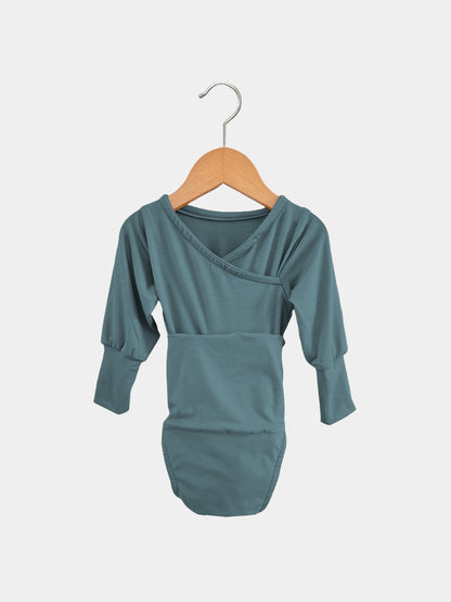 Der Loopbody Bambusviskose - Ozean zeigt einen langärmeligen, mitwachsenden Babybody in gedecktem Türkis mit Umschlaghals. Er hängt an einem Holzkleiderbügel vor einem schlichten Hintergrund.