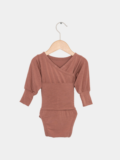 Loopbody Kaschmir-Mix - mitwachsender Babybody - Zimt: Langarm-Body mit Wickeloptik, leicht gerafften Ärmeln und Druckknopfverschluss, aus superweichem Kaschmir-Mix, auf einem einfachen Holzkleiderbügel präsentiert.