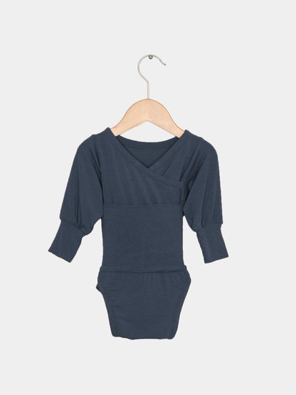 Loopbody Kaschmir-Mix - Blaubeere: Langarm-Babybody mit Wickelausschnitt, an einem Holzkleiderbügel hängend. Der Body ist aus weichem Kaschmir-Mix, ohne Knöpfe, ideal für zarte Babyhaut.