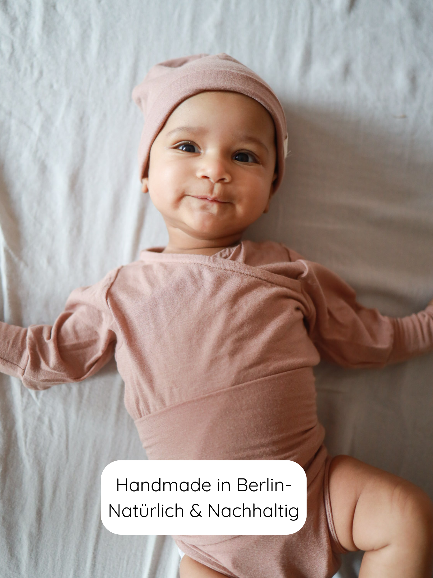 Ein Baby trägt den Loopbody Kaschmir-Mix - Puder, einen weichen, langärmligen Body aus Kaschmir-Mix mit einzigartigem Loop-Design, das Wärme spendet und einfaches An- und Ausziehen ermöglicht.